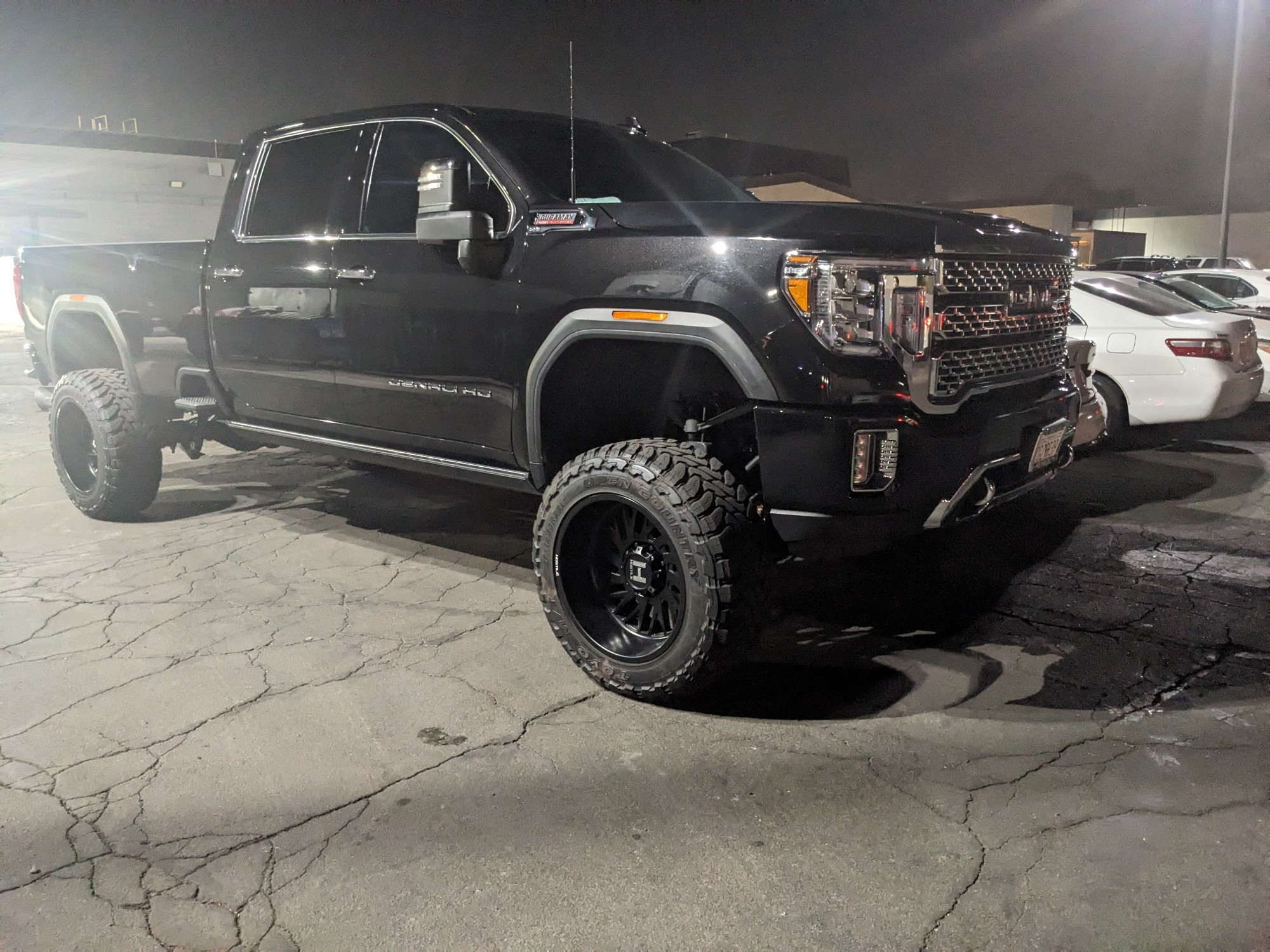 a slightly distant side profile view of a gigantic GMC pickup trick. it is lifted with a hood easily over 6 feet tall.