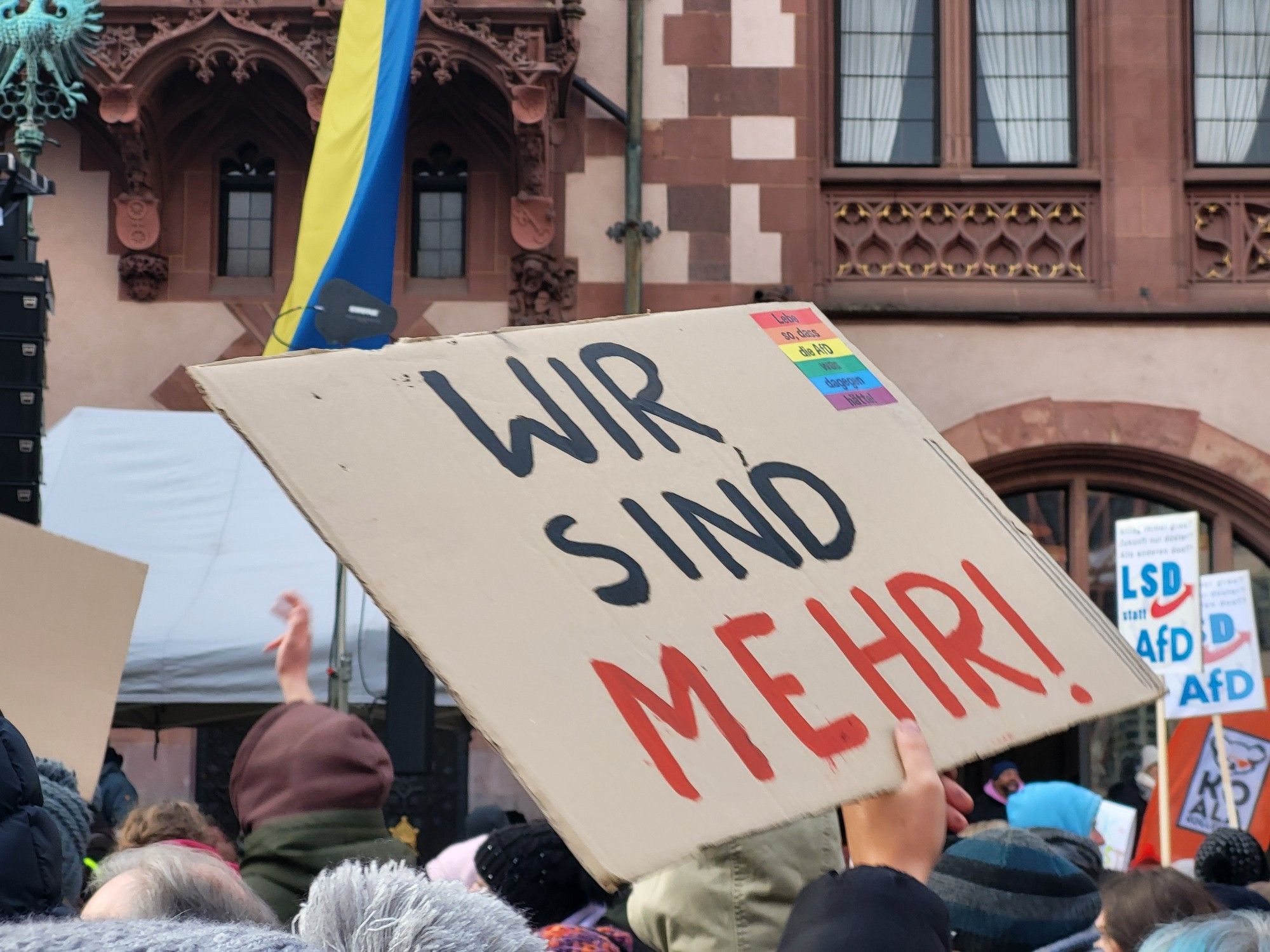 Plakat auf der Demo gegen AfD und Rechtsextremismus. Zu sehen ist ein hochgehaltenes Pappplakat, auf dem "Wir sind mehr!" steht.