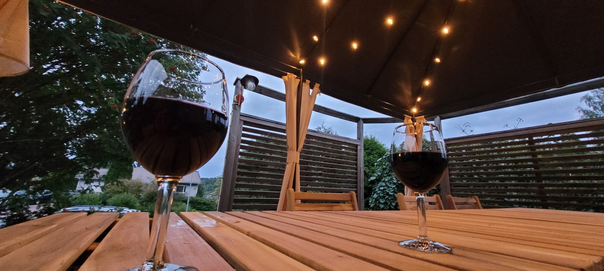 Two glasses of red wine on the picnic table on our deck under gazebo and lights.