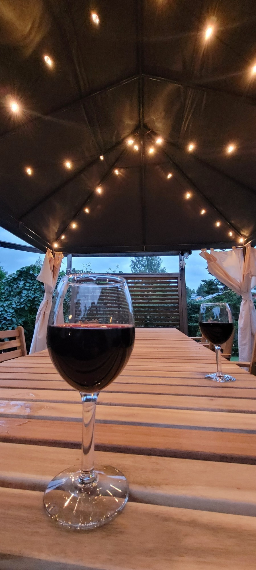 Two glasses of red wine on the picnic table on our deck under gazebo and lights.