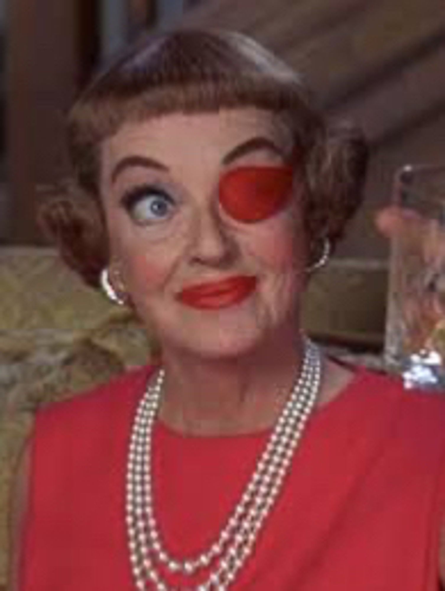 Bette Davis wearing pearls, an eyepatch and a red blouse