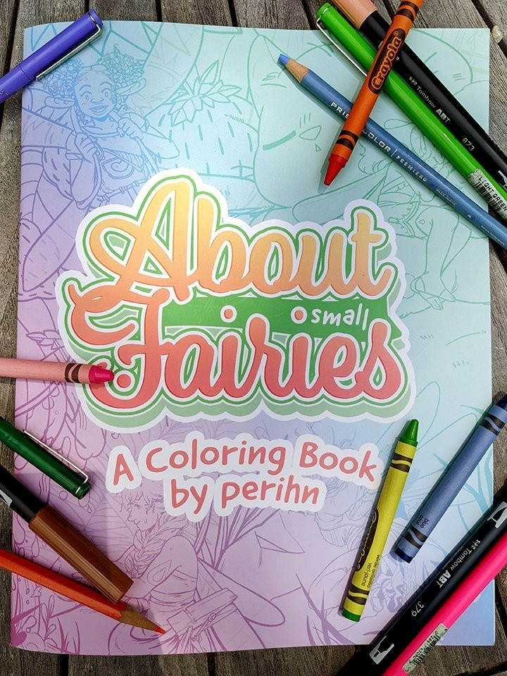 Photo of a rainbow gradient book cover, titled "About Small Fairies - A Coloring Book by perihn" surrounded by different drawing tools; crayons, markers, pens and colored pencils.