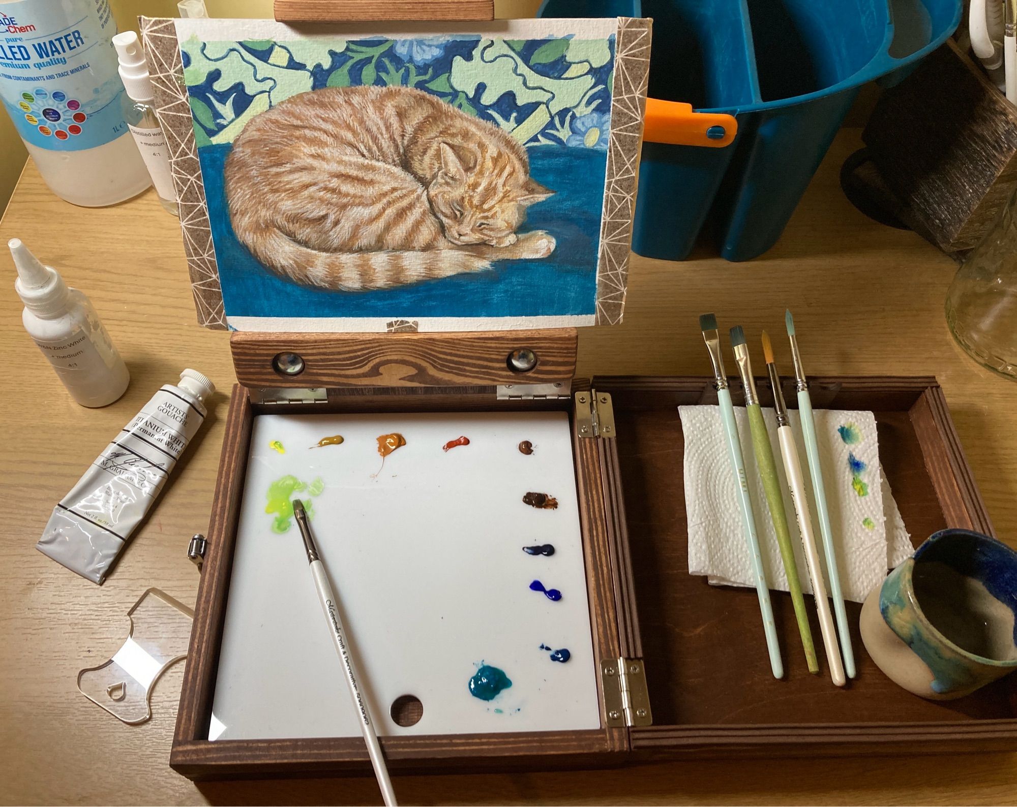 Wooden pochade box with brushes, palette and painting of a ginger tabby cat in progress