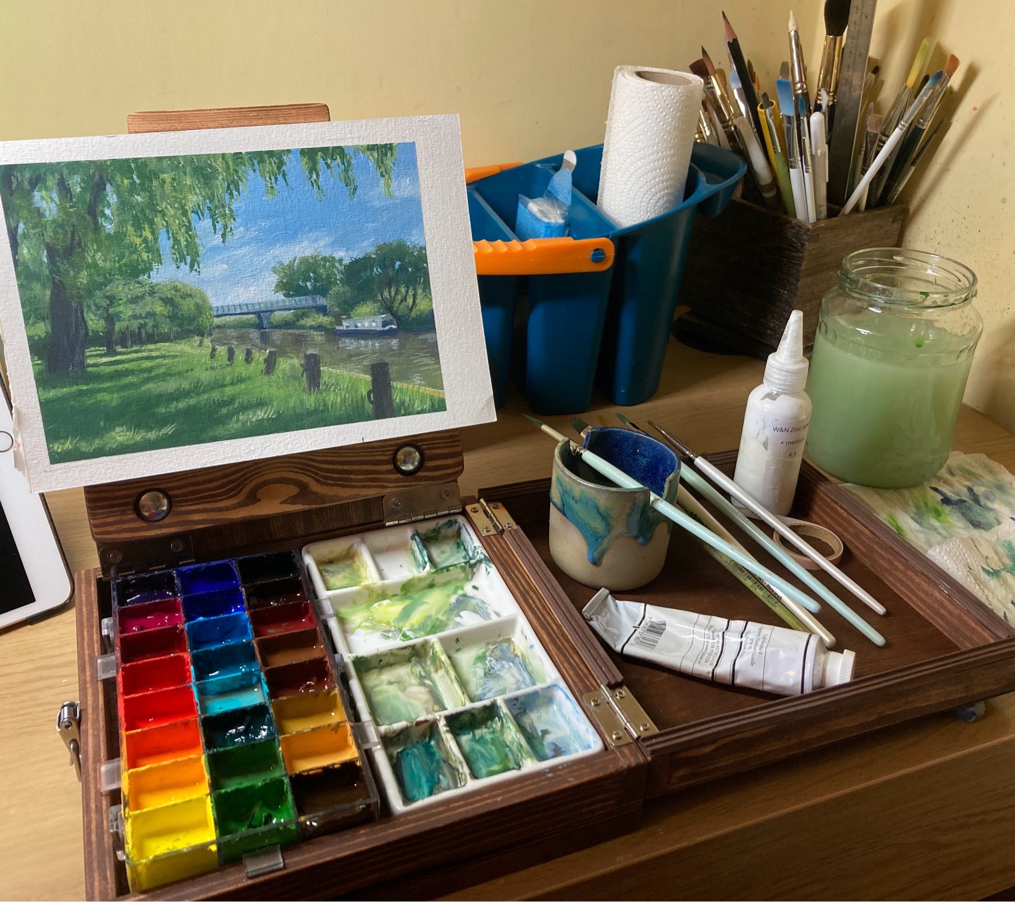 Gouache landscape painting in a wooden pochade box with paints, palette and brushes