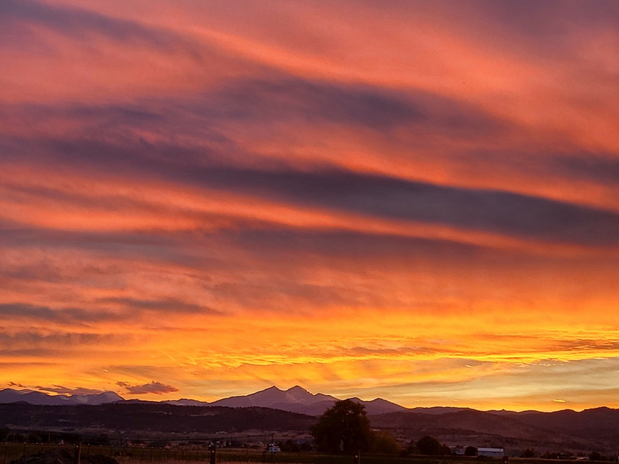 Very colorful layers of orange and yellow sunset clouds in the sky above a mountain range.