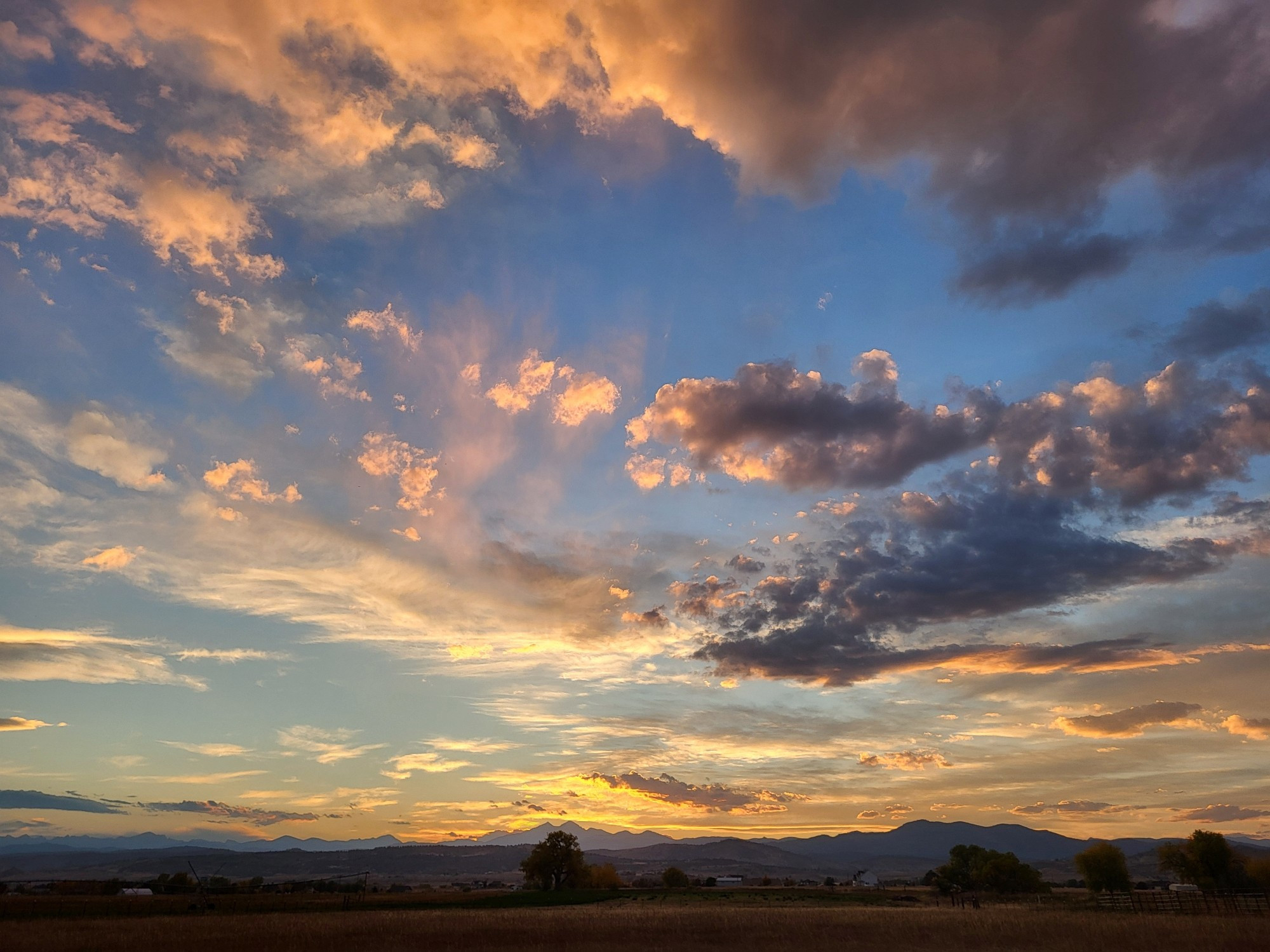 At the bottom of the frame is a line of mountains. Above is a sky filled with clouds colored by the sunset.