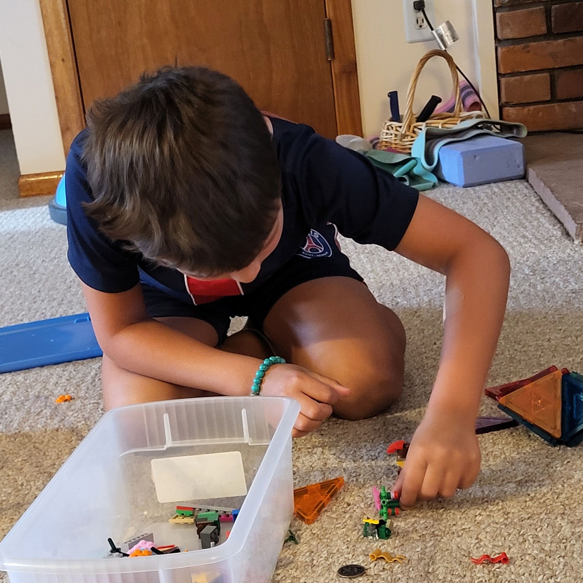 A young boy bent over Legos on a carpet.