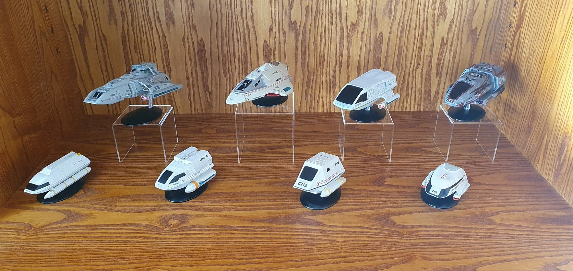 Series of Eaglemoss models of shuttlecraft from Star Trek displayed on a timber shelf. Top row (L to R): Runabout (DS9), Delta Flyer (VOY), Shuttlecraft Yosemite (LWD), and C-Class shuttle (DIS). Lower row (L to R) Cargo Shuttle (TNG tech manual), Type-6 shuttlecraft Goddard (TNG), Type-15 shuttlepod El-Baz (TNG), and Type-7 shuttle Hawking.