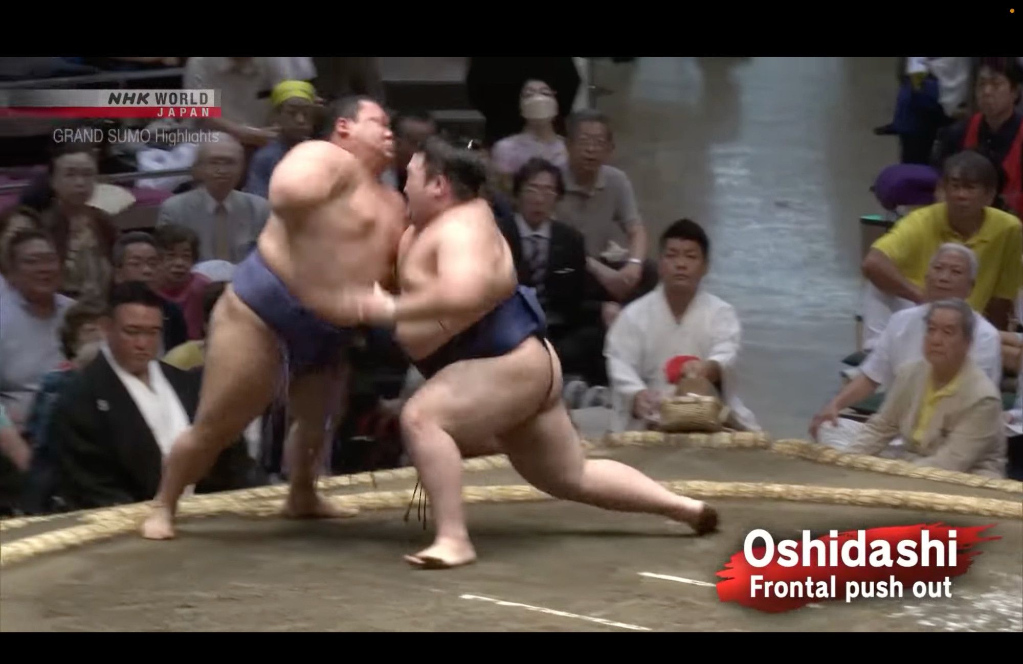 A sumo wrestler attacks his opponent with a deep lunging drive