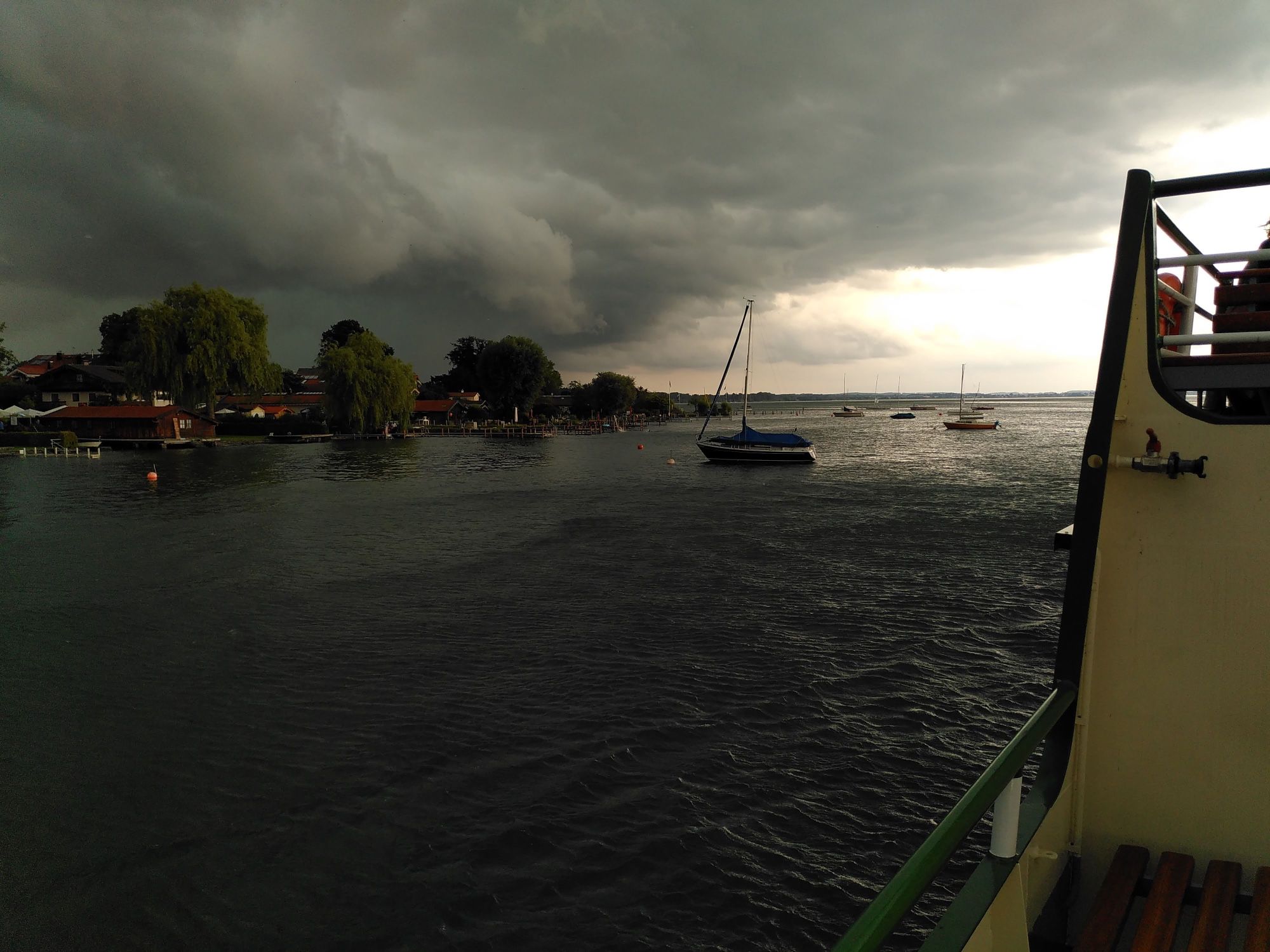 'Vor dem Sturm' #FotoVorschlag.

Foto des Chiemsees vor einem Sturm am 28. Juli 2021. Zu sehen sind dunkle Wolken, das fast schwarze Wasser, ein kleiner Hafen mit Bäumen am Ufer und einzelne Boote.