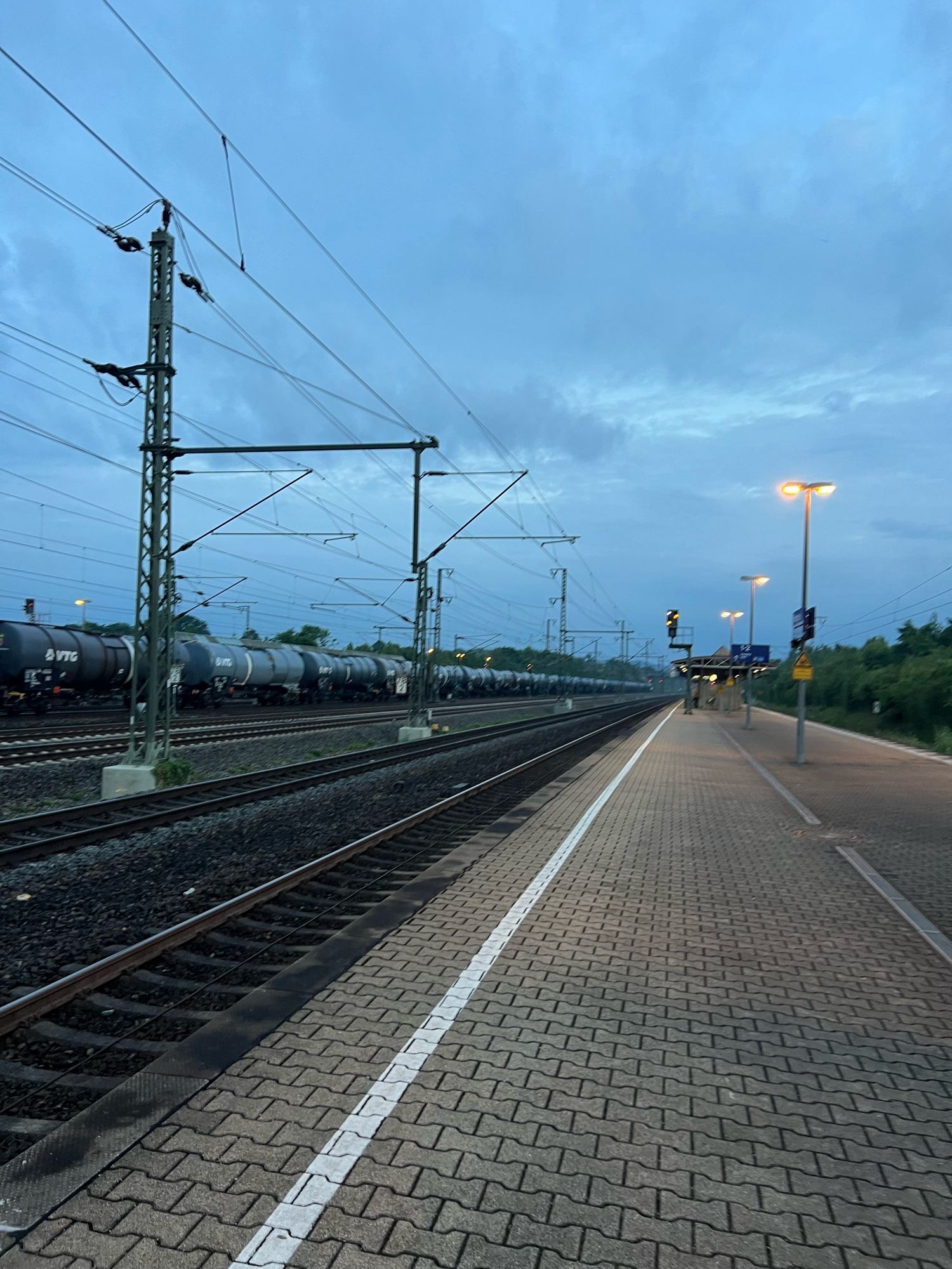 Bahngleis mit grauen Knochensteinen und mittig Straßenlaternen. Rechts die Schienen