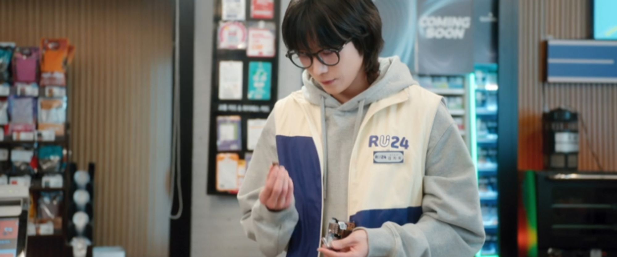 A man with shoulder length hair and nerd glasses stares lovingly at one of the Kopiko sweets while standing in a convenience store.