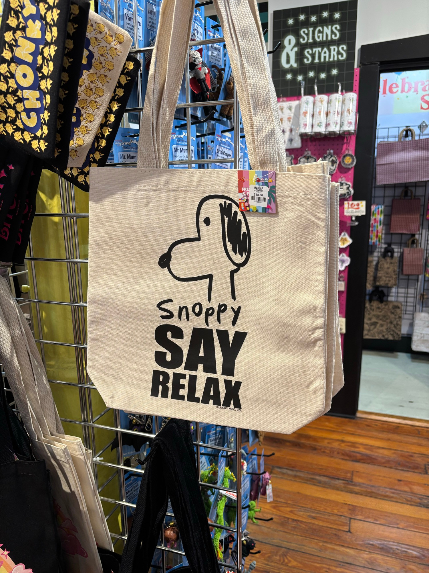 a tote bag in a gift shop with a crude drawing of snoopy. Text: “Snoppy SAY RELAX”