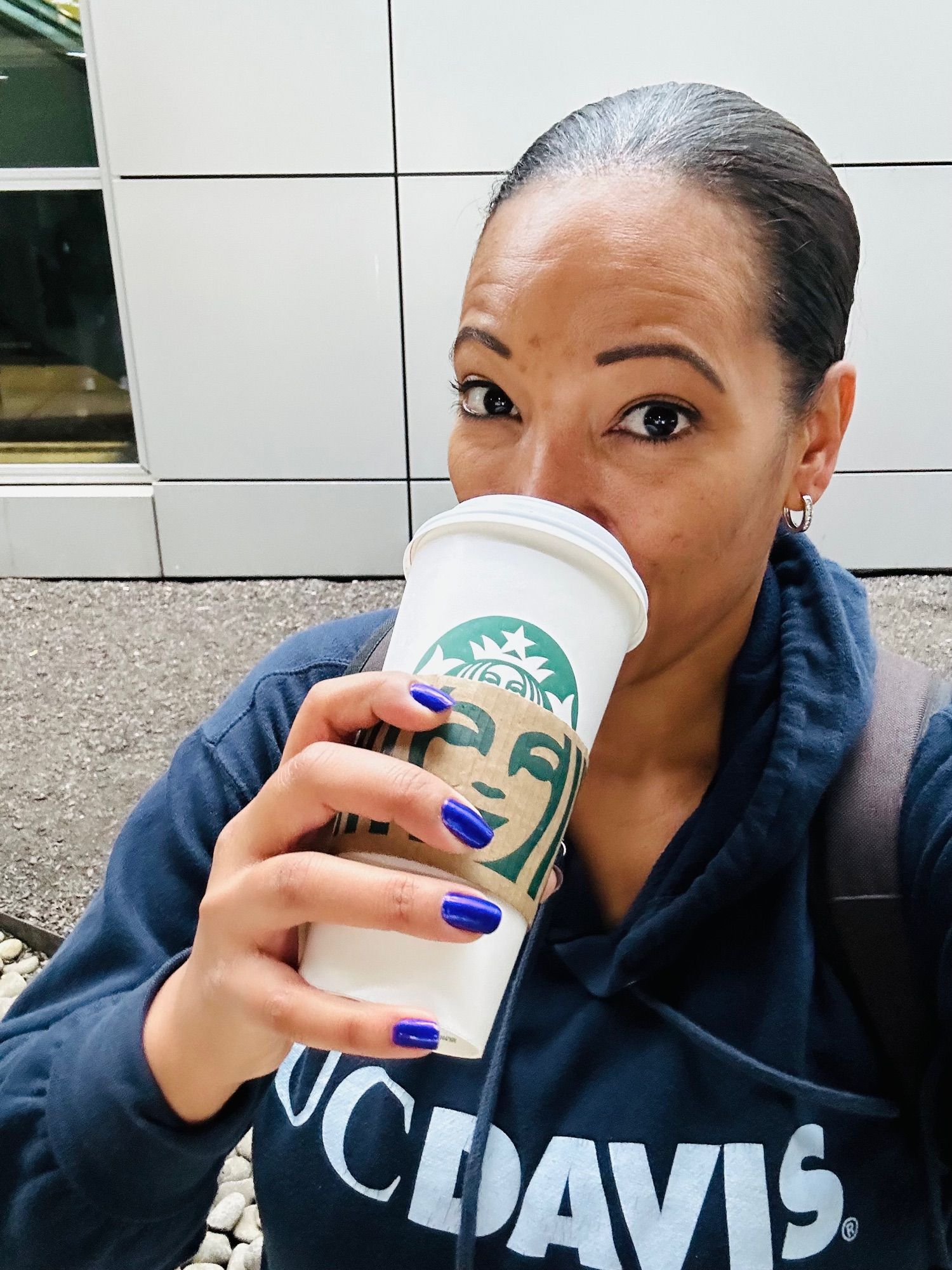 Woman in a UC Davis sweatshirt chugging a venti Starbucks at the Boston airport after a red eye flight.