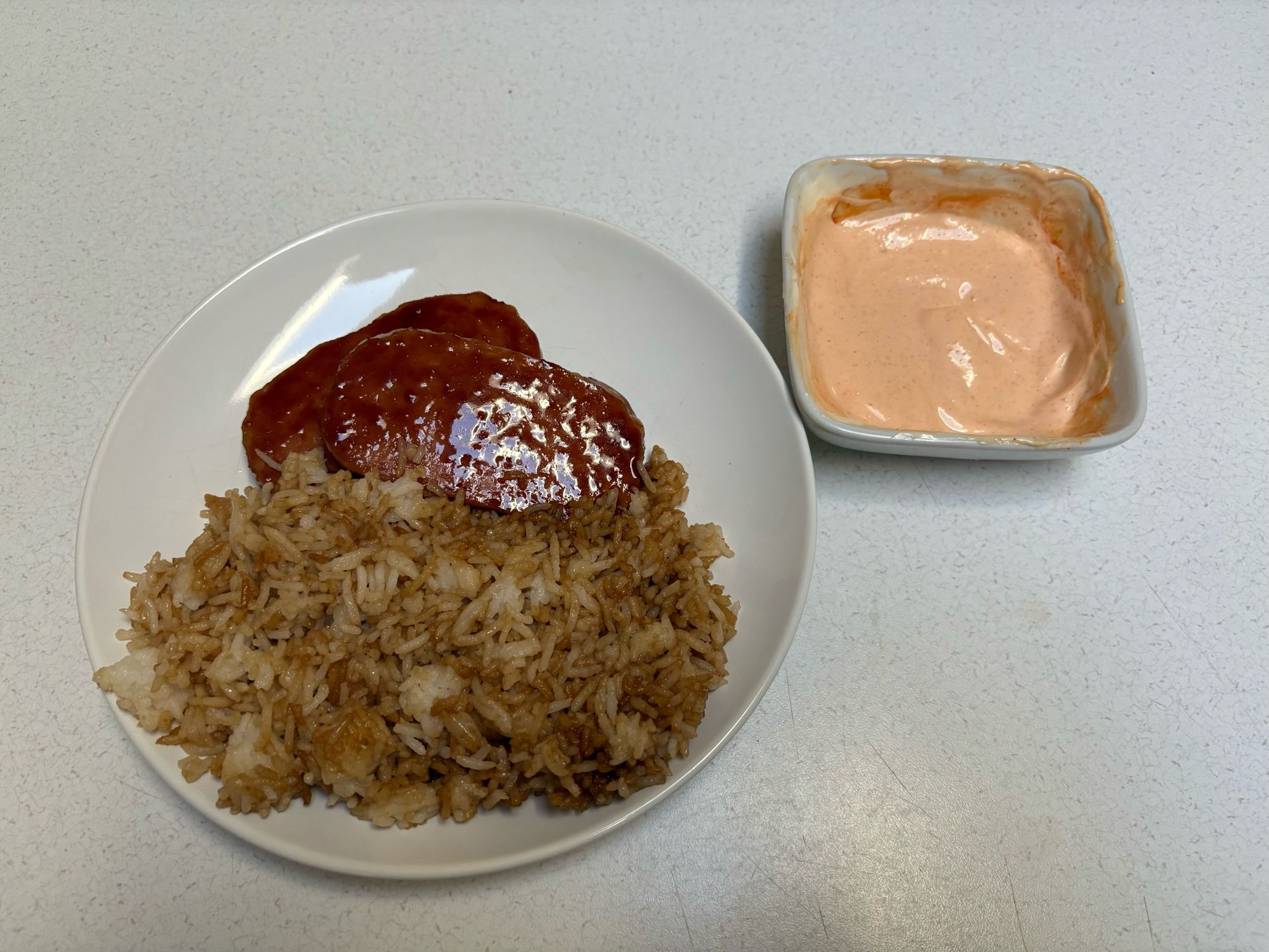 Fried spam with a teriyaki glaze and fried rice on a plate with a side of spicy garlic mayo dipping sauce.