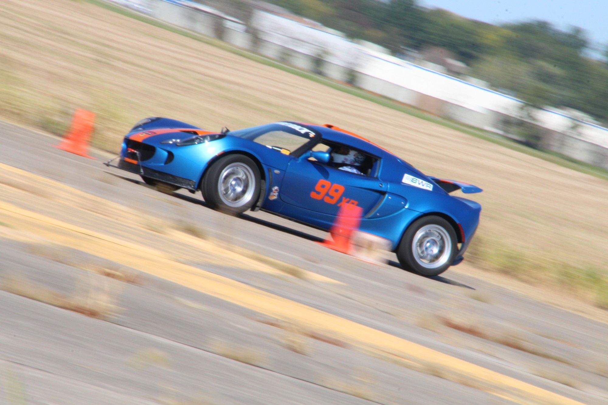 A blue with orange stripe Lotus Elise on course.