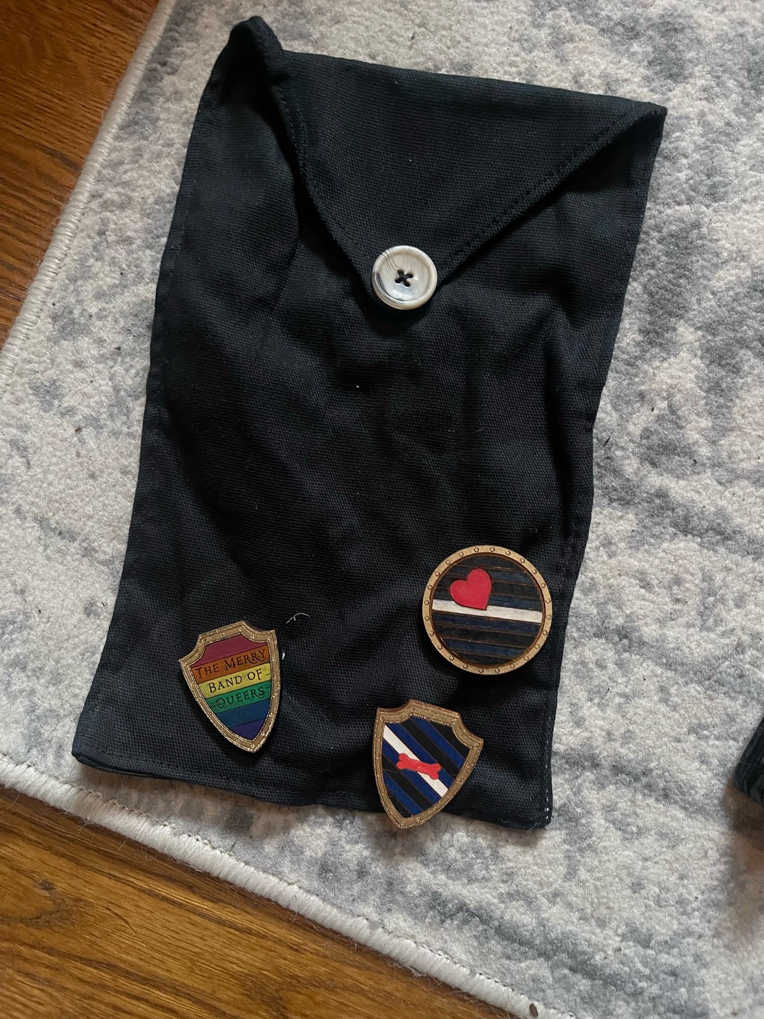 A fabric pin sash with three pins, one rainbow pin that says “the merry band of queers”, one with the pup flag, and another with the leather flag.