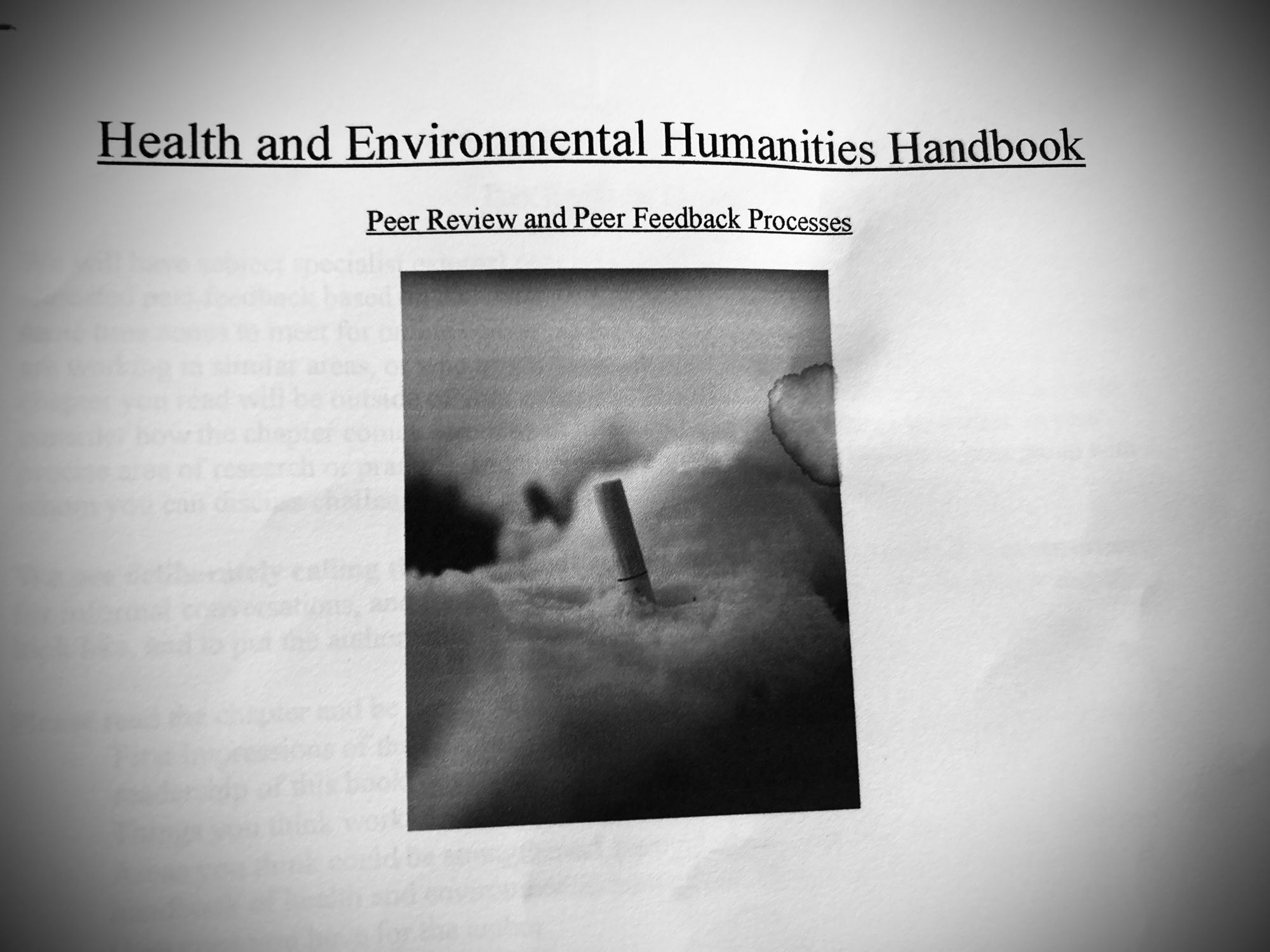 Text on a sheet of paper, reading “Health and Environmental Humanities Handbook. Peer review and peer feedback process.” A black and white photograph underneath.