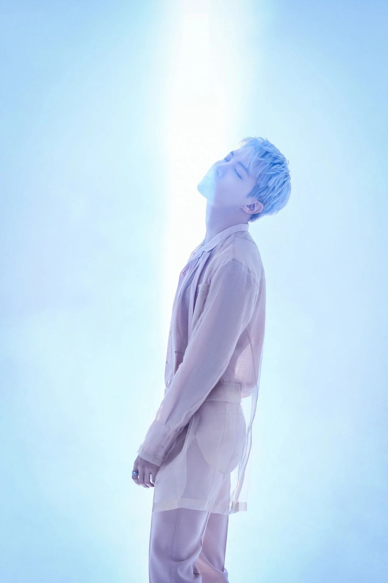 J-Hope from the Proof concept photos from 2022. He's wearing soft pink while a blue-ish beam of light illuminates him from behind