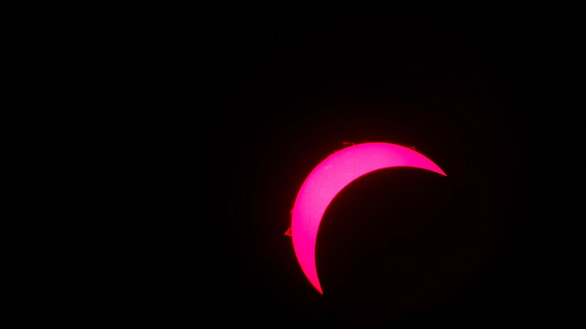 A 30% solar crescent in H-alpha lens, taken with a cellphone. Prominences are visible on the edge of the sun.