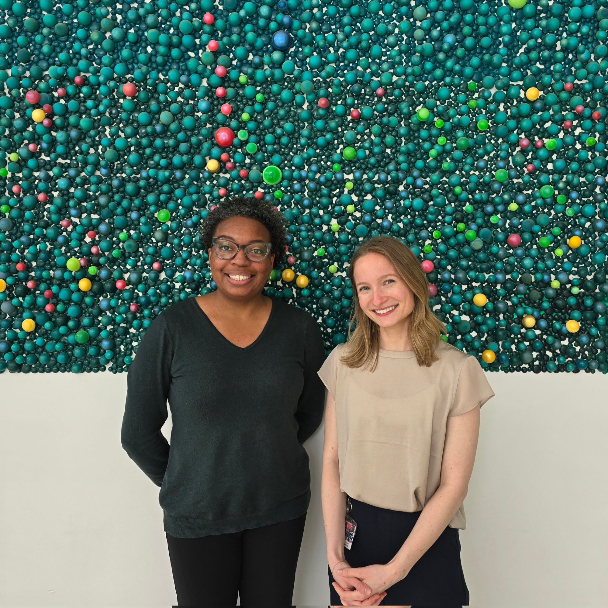 Maren and Erica smiling together. A green textured wall is in the background.