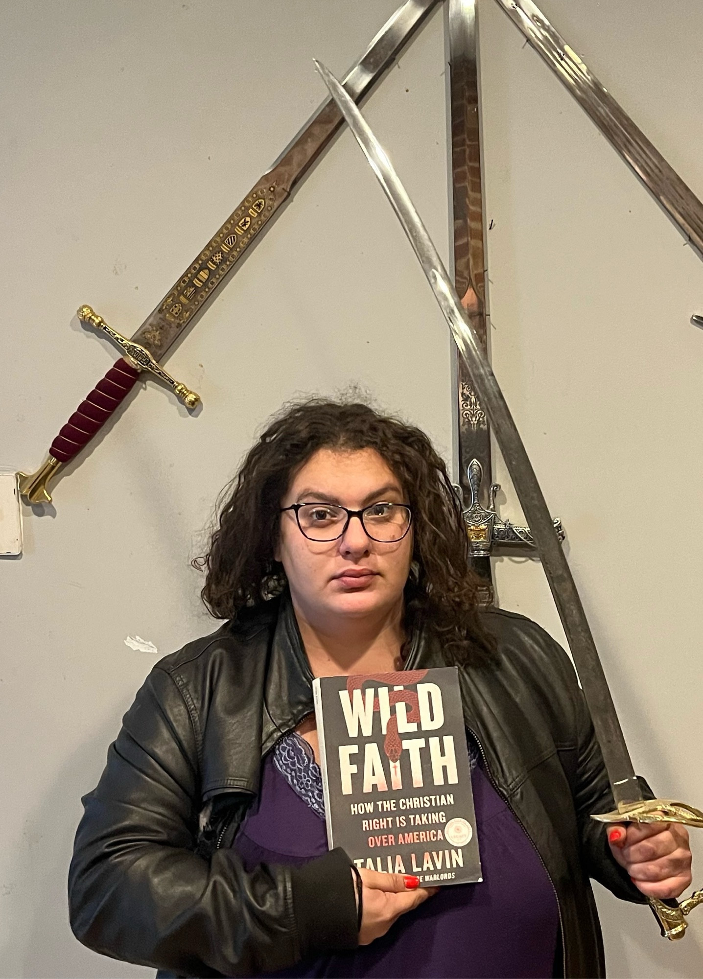 a crazed looking talia wields a saber & her book wild faith