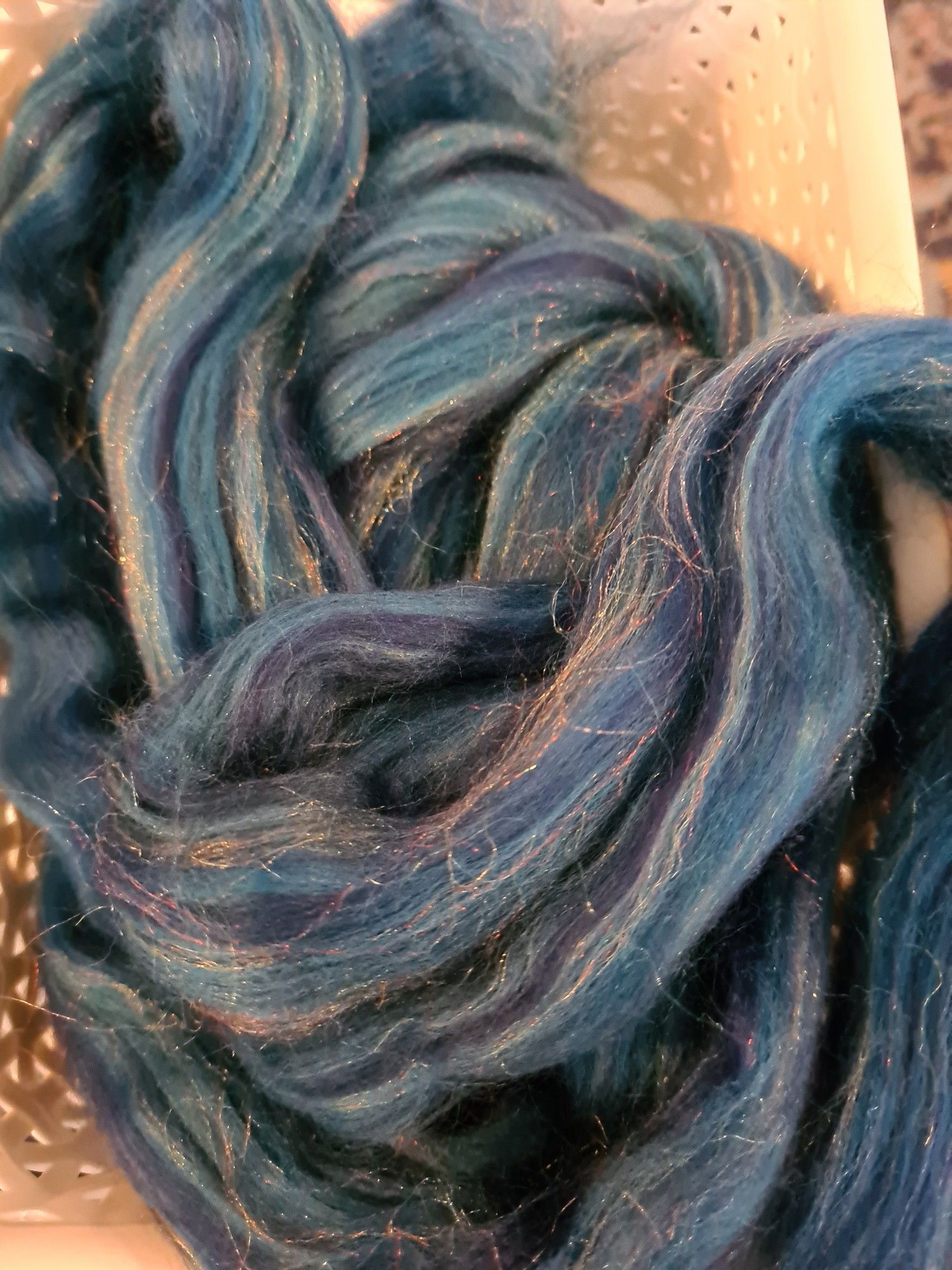 Multiple shades of blue and teal unspun Corriedale wool blended with fine threads of rainbow shiny nylon. It is a blend called Peacock from World of Wool.