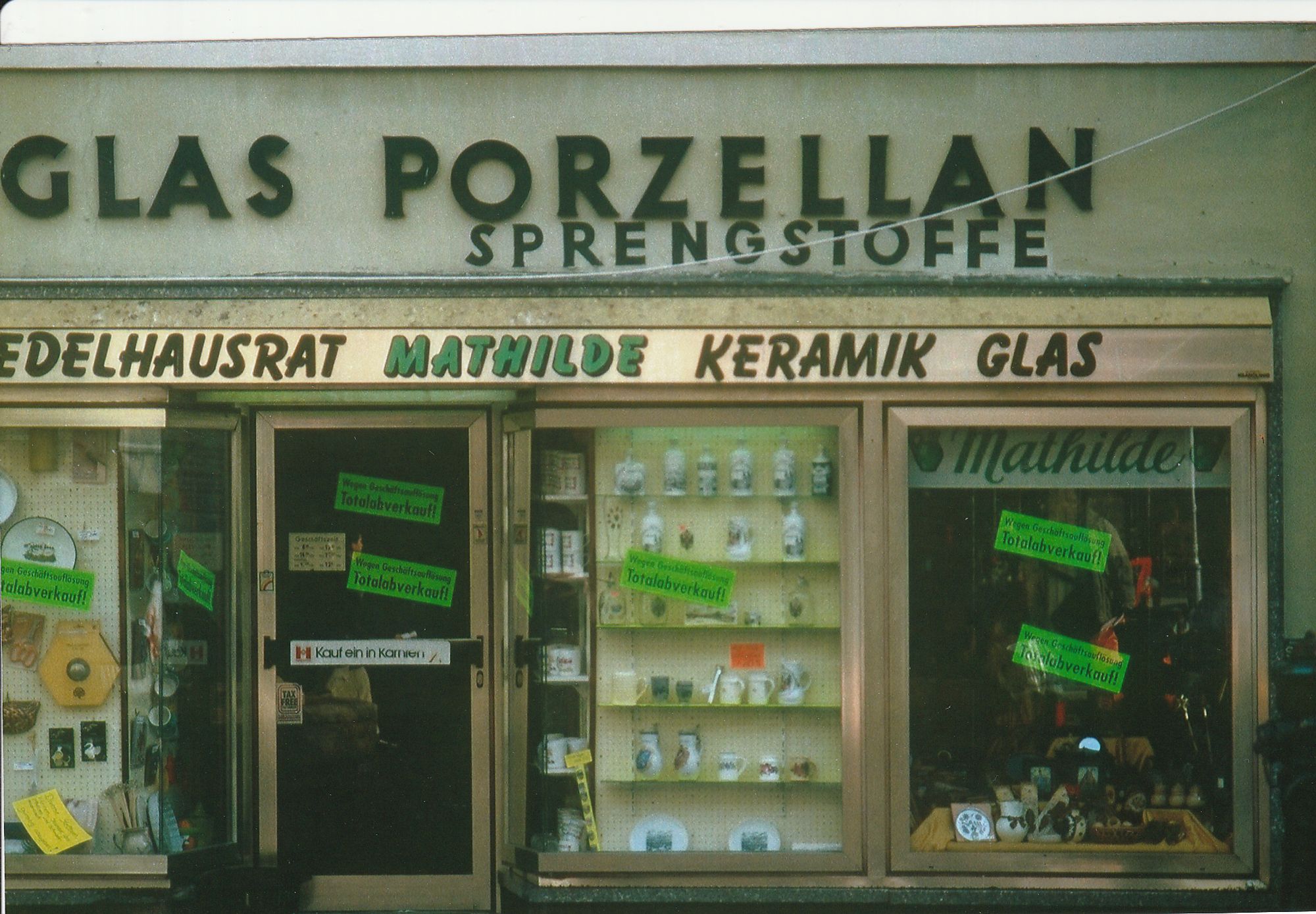 Ein altes Foto eines Auslage eines Souvenir-Geschäfts. Oben steht "Glas Porzellan" darunter steht "Sprengstoffe"