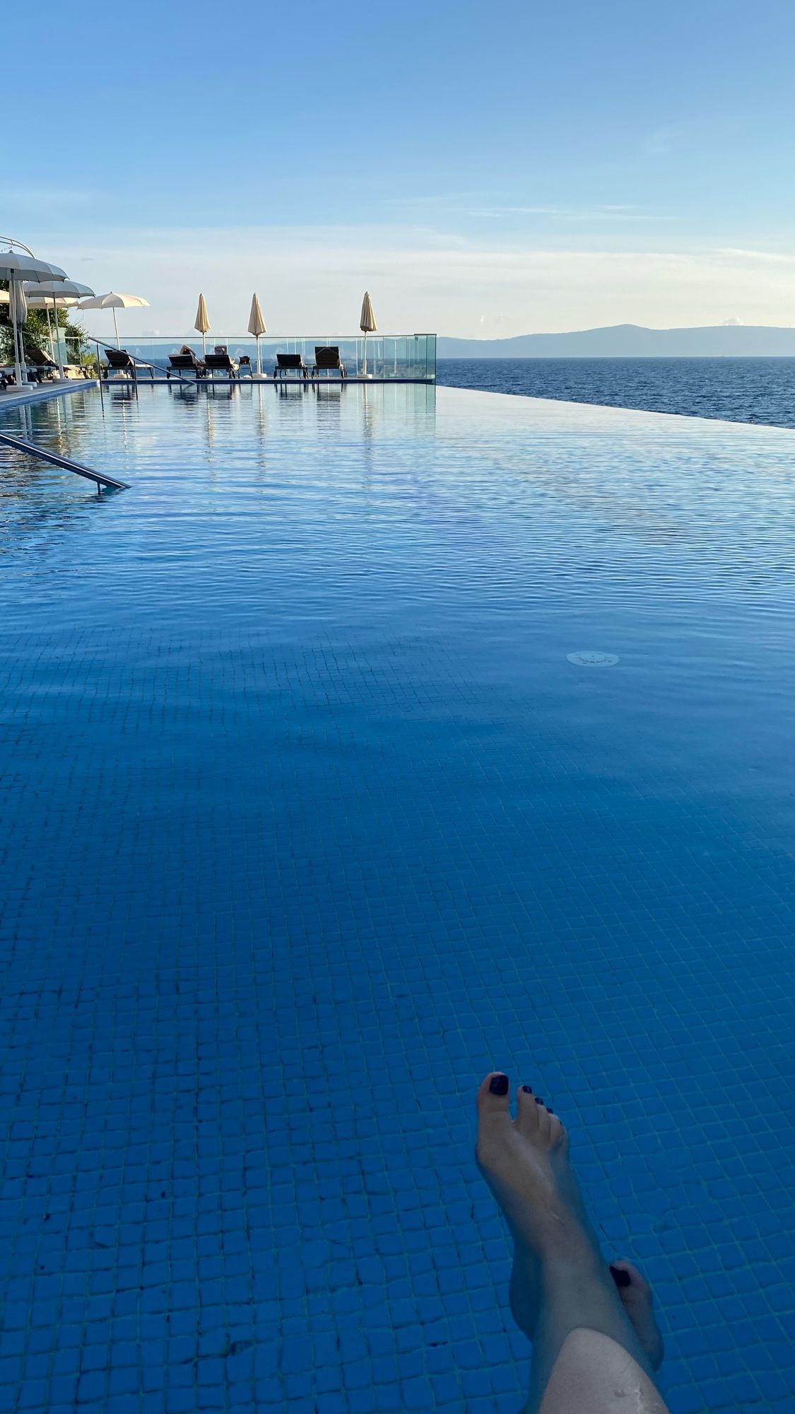 Ein  Infinitypool mit Block aufs Meer. Es sieht wie ein nahtloser Übergang aus. Am unteren Rand von Bild sind meine Füße im Wasser zu sehen.