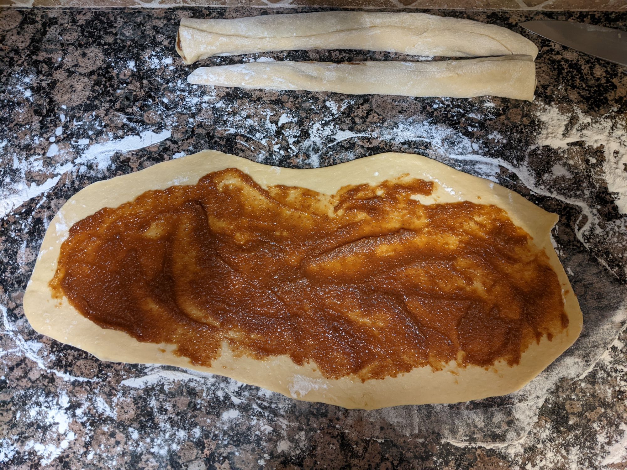 Challah dough rolled out and spread with fig filling, and two ropes of dough  that have already been rolled after being filled with fragrant orange zest-fig paste