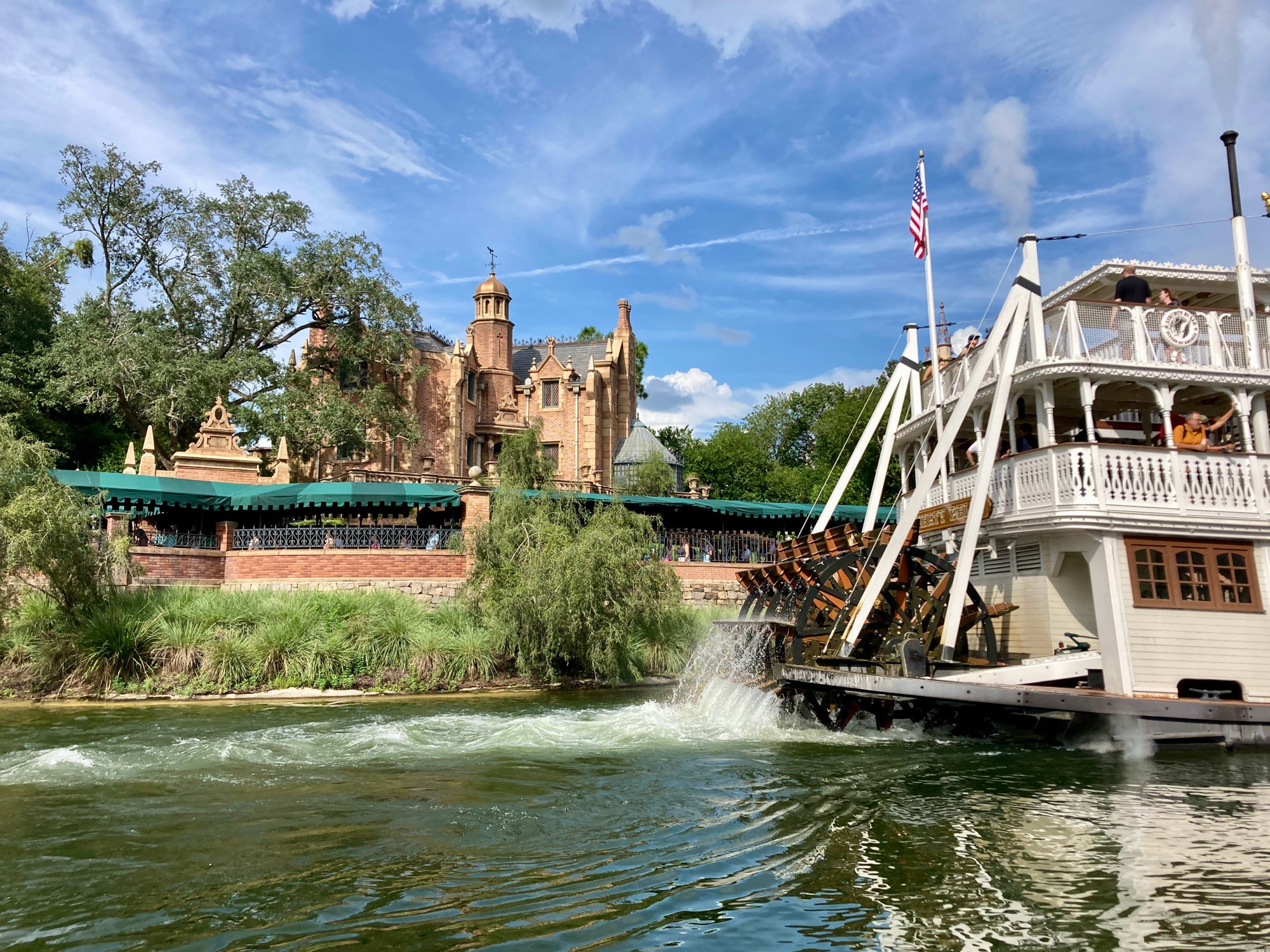 The Haunted Mansion at Magic Kingdom as seen from Tom Sawyer Island with the Liberty Belle riverboat passing by, and of course a blue sky in the background