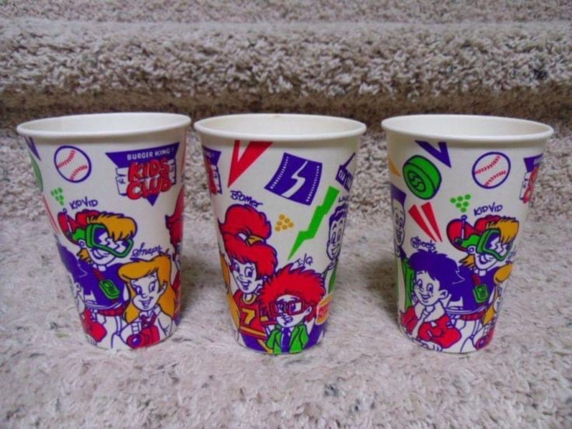 Burger King Kids Club paper cups from the 90s. Design is white with bright colorful cartoon kids and various details like a baseball, a lightning bolt, triangles and dots.