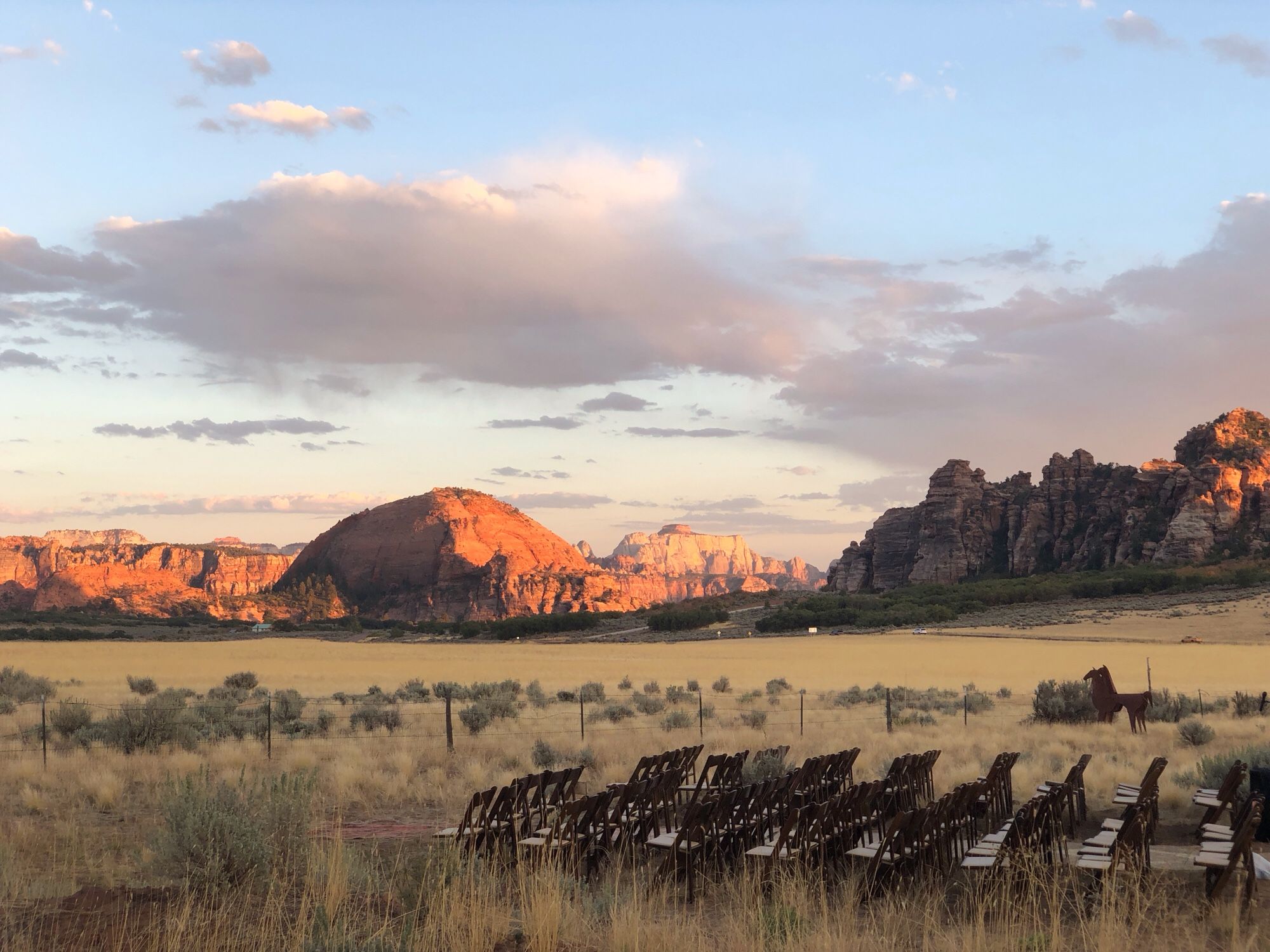 The wedding site in Virgin, Utah. There are some chairs arranged in a field covered with prairie grass and sagebrush. In the background are some amazing rock formations of reddish orange sandstone