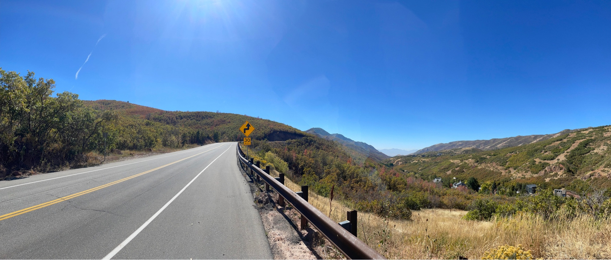 A canyon road approaching a switchback. Golden grass and slightly orange-tinted bushes and trees on either side