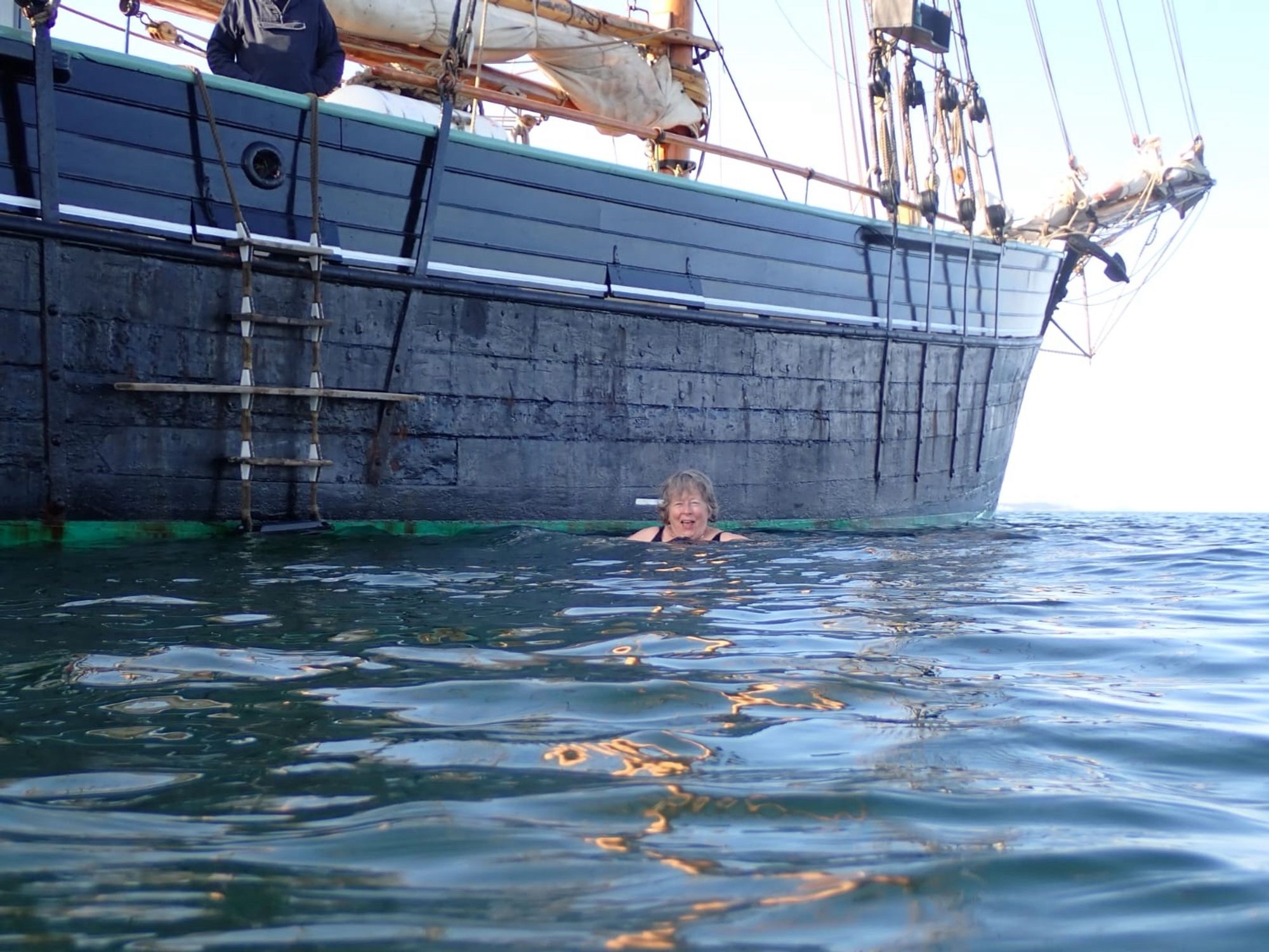 A swimmer in the sea beside a wooden ketch, called the Bessie Ellen.