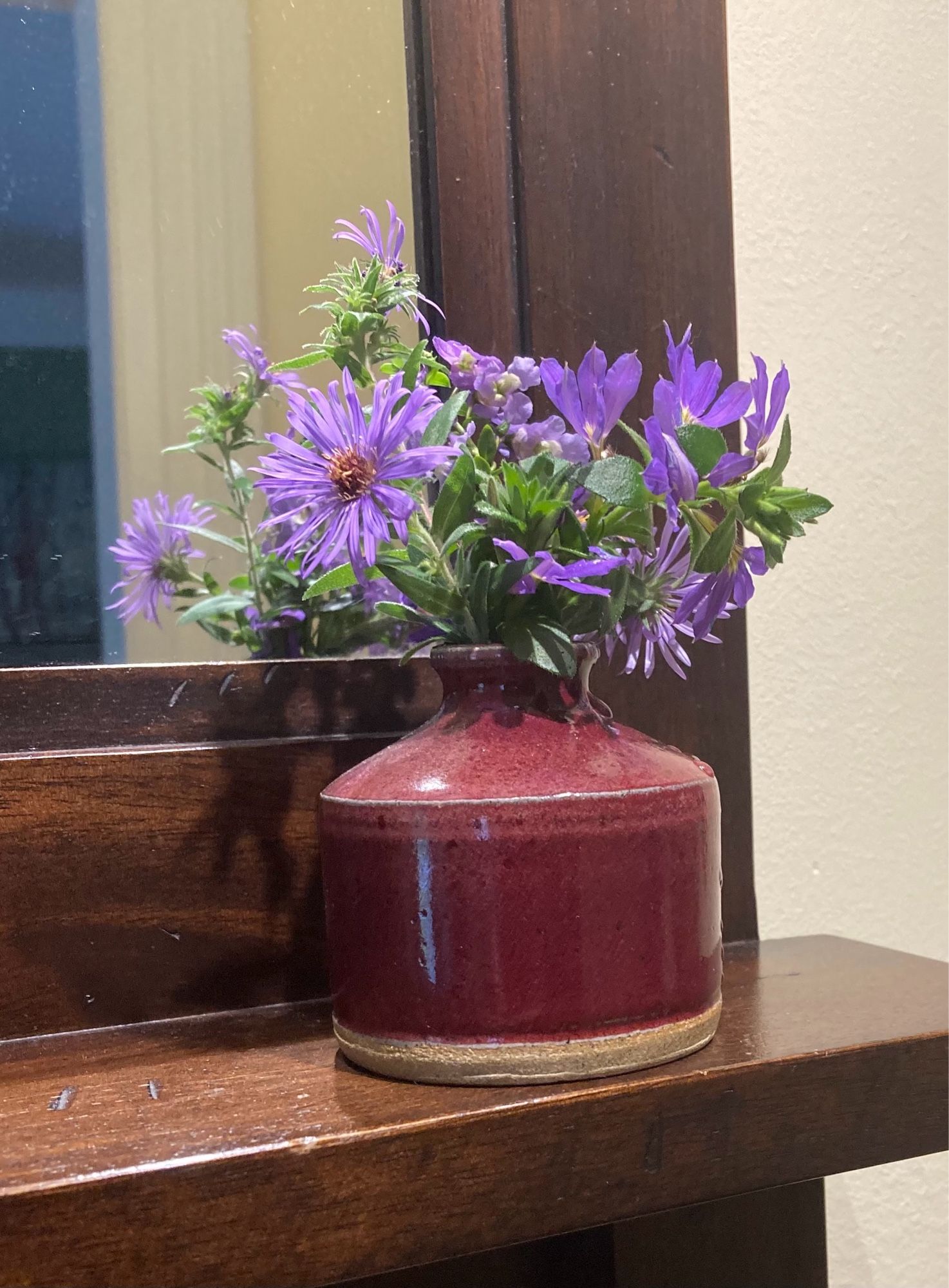 Small pottery vase with three types of purple flowers, including asters.