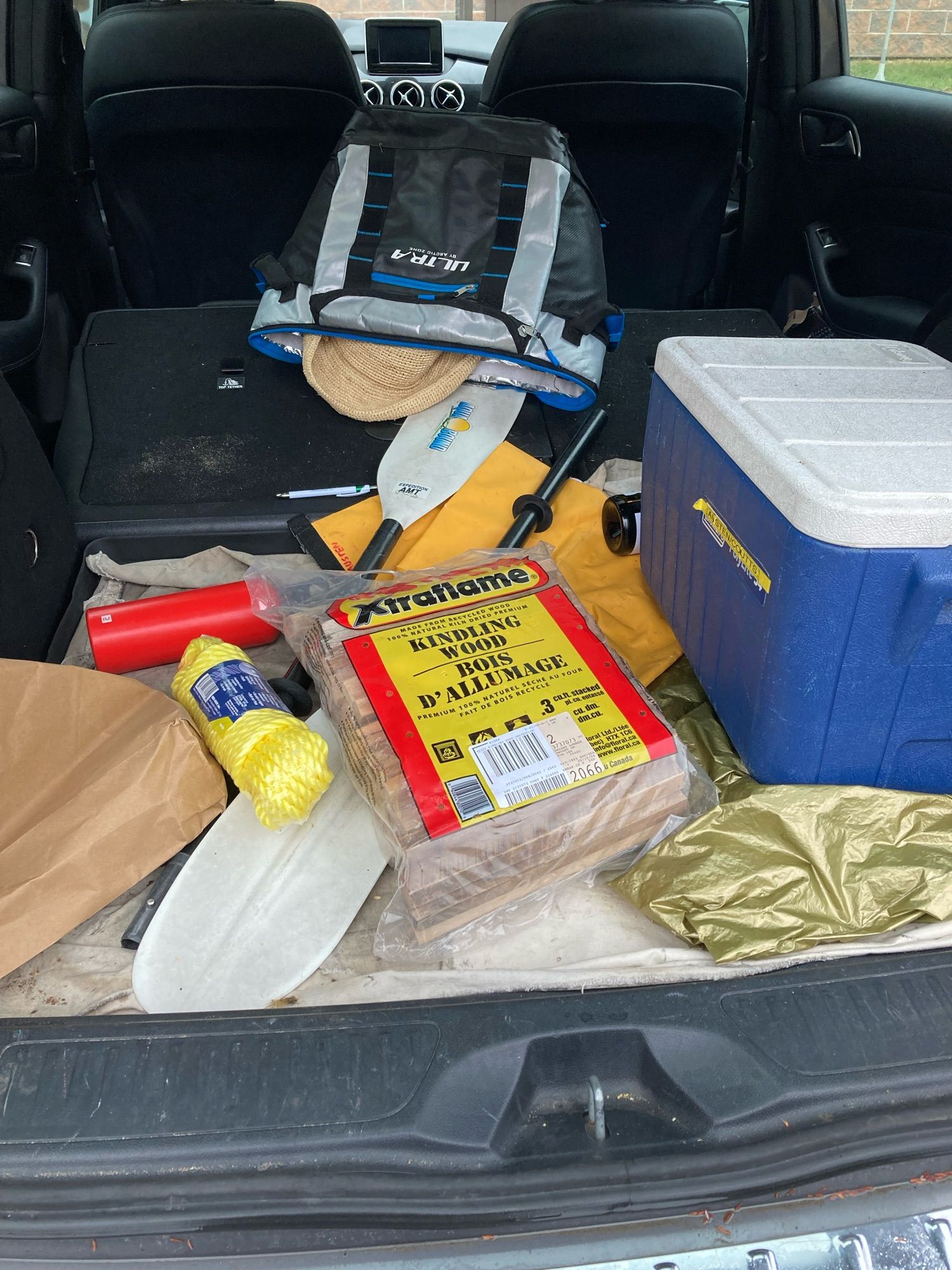 Car full of summer junk. Kindling, a paddle, a sun hat, a cooler, a dry bag from canoeing, yellow rope, a water bottle.