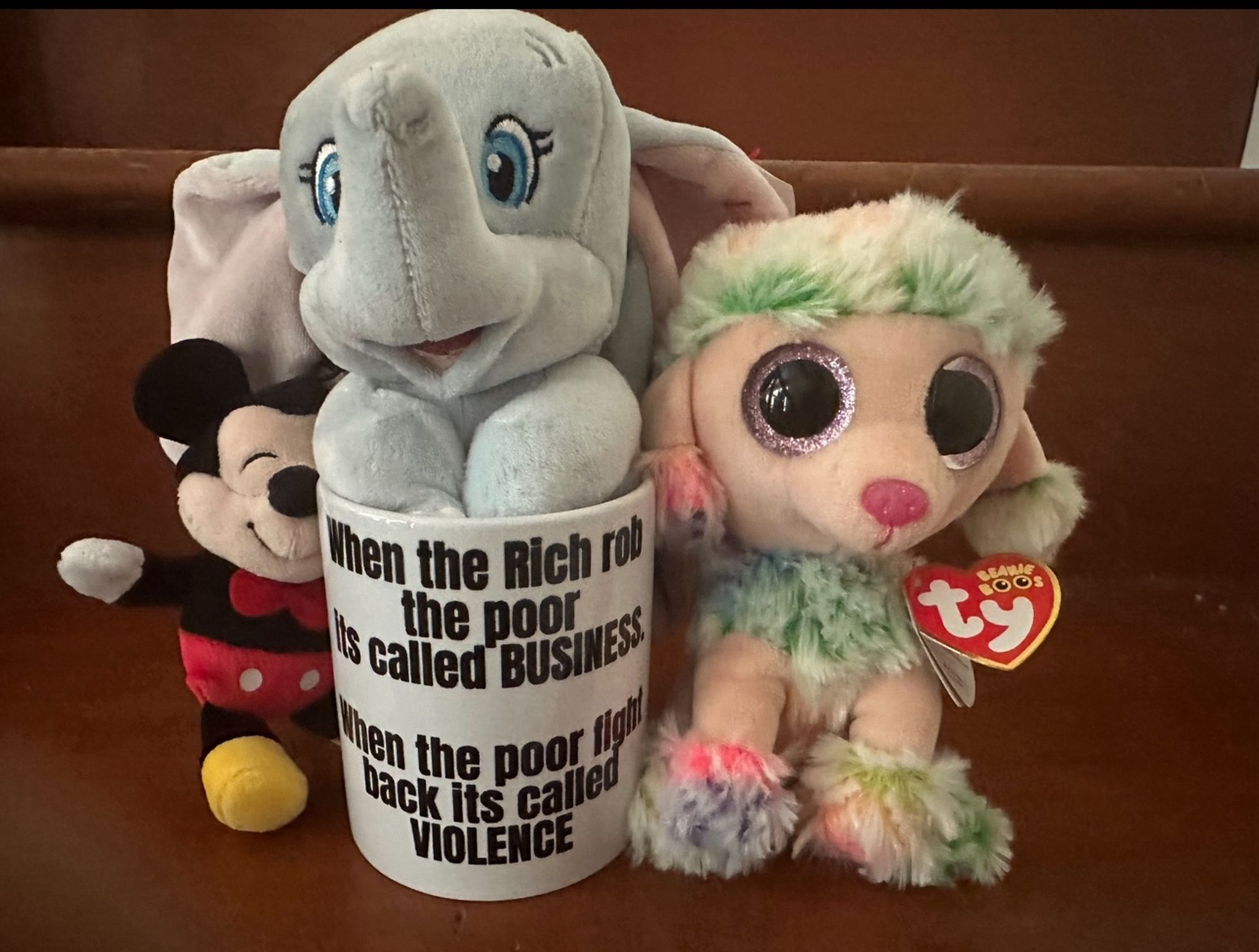 When the Rich rob the poor is called BUSINESS. when the poor fight back it’s called 
VIOLENCE ( Dumbo sits in a cup saying that) 

Mickey Mouse beside him and a big eyed doll next to him