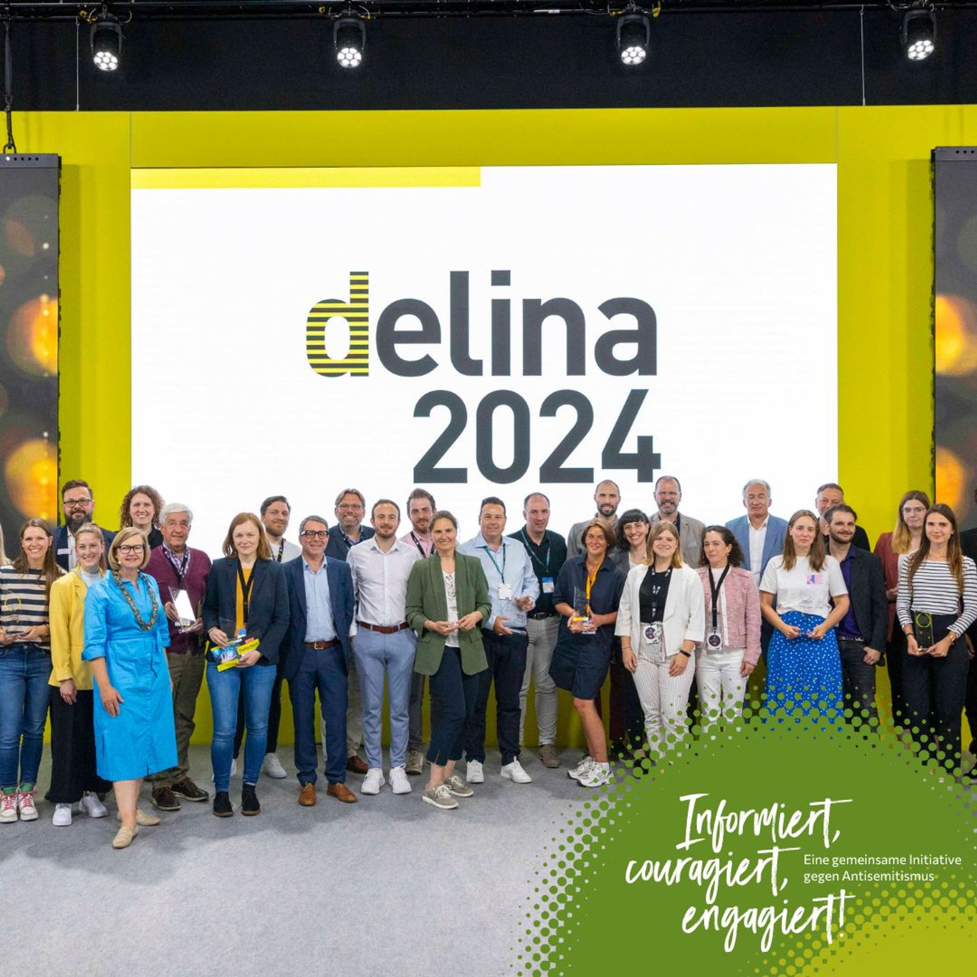 eine Gruppe von Menschen steht vor einem großen Bildschirm. Auf diesem steht "delina 2024".