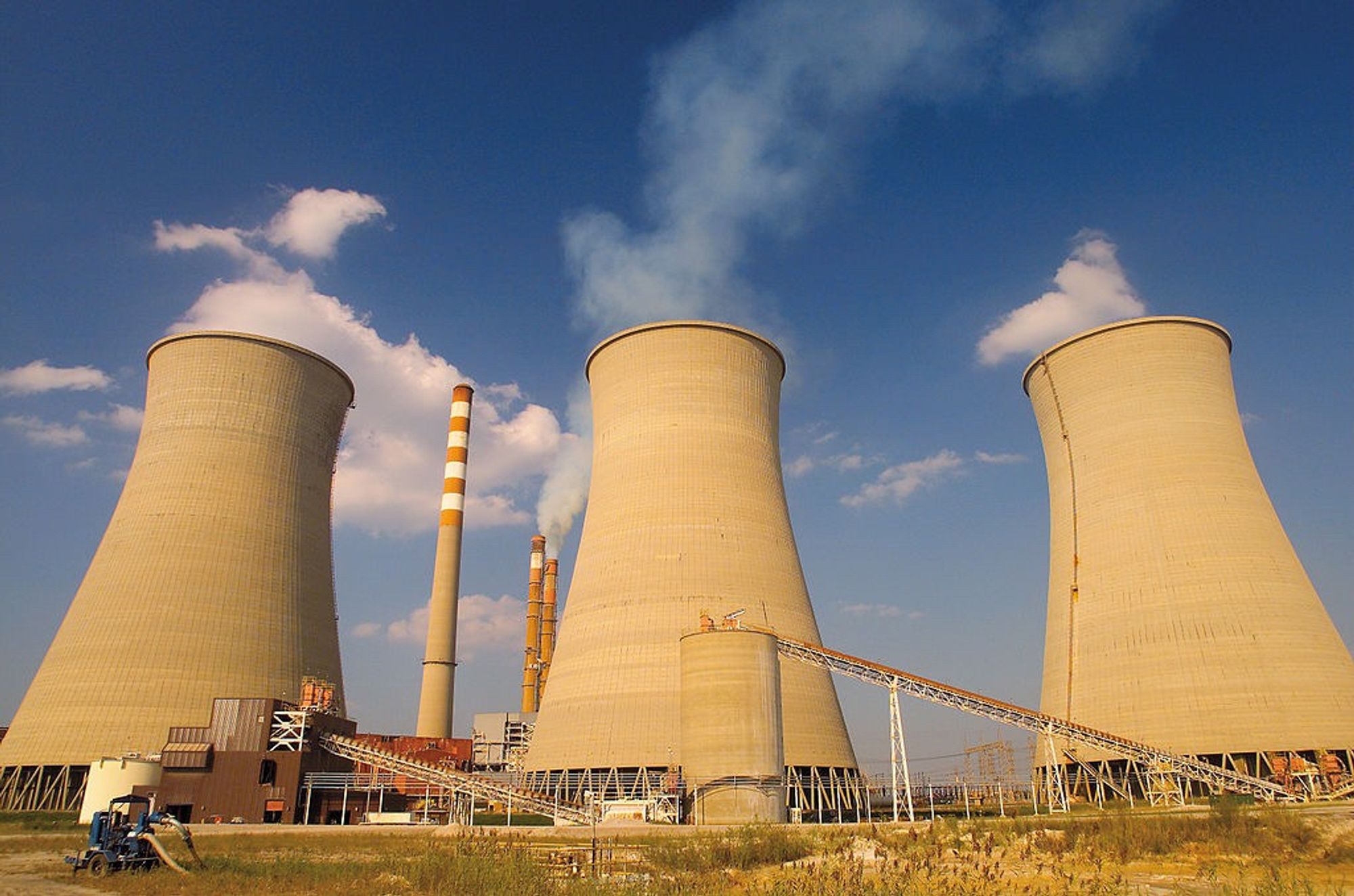 The Paradise fossil fuel plant in Paradise, KY is shown with three enormous cooling towers and smokestacks in the background against a blue sky with scattered clouds. Source: Wikimedia Commons.