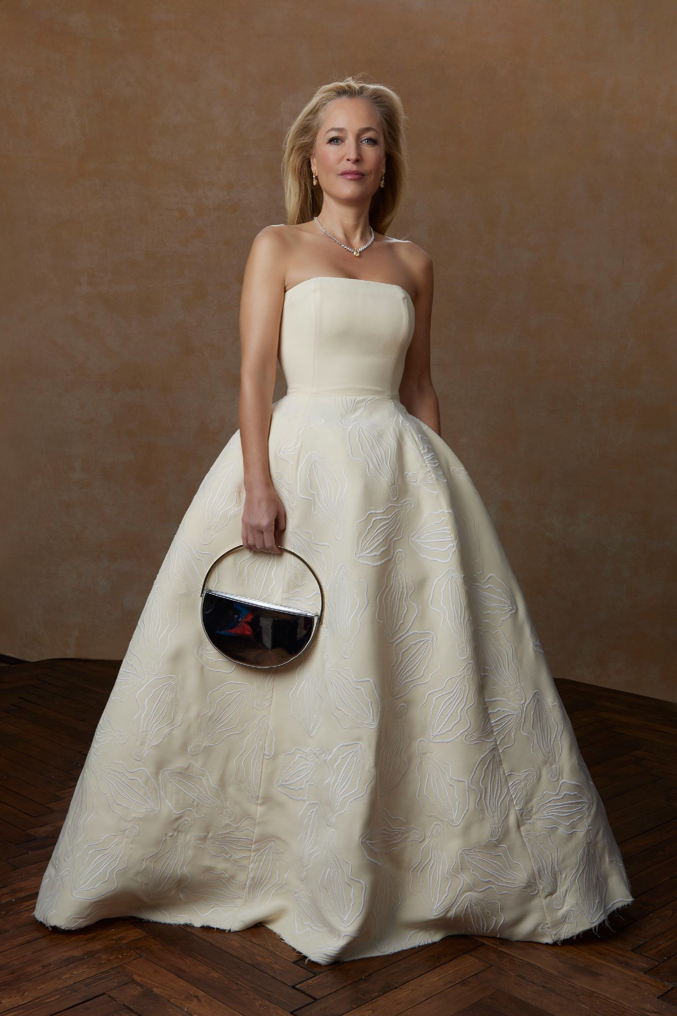 Picture of Gillan Anderson at the Golden Globes, wearing what looks like a plain ivory strapless evening gown. Looking closer, you can see many embroidered vulvas on the fabric.