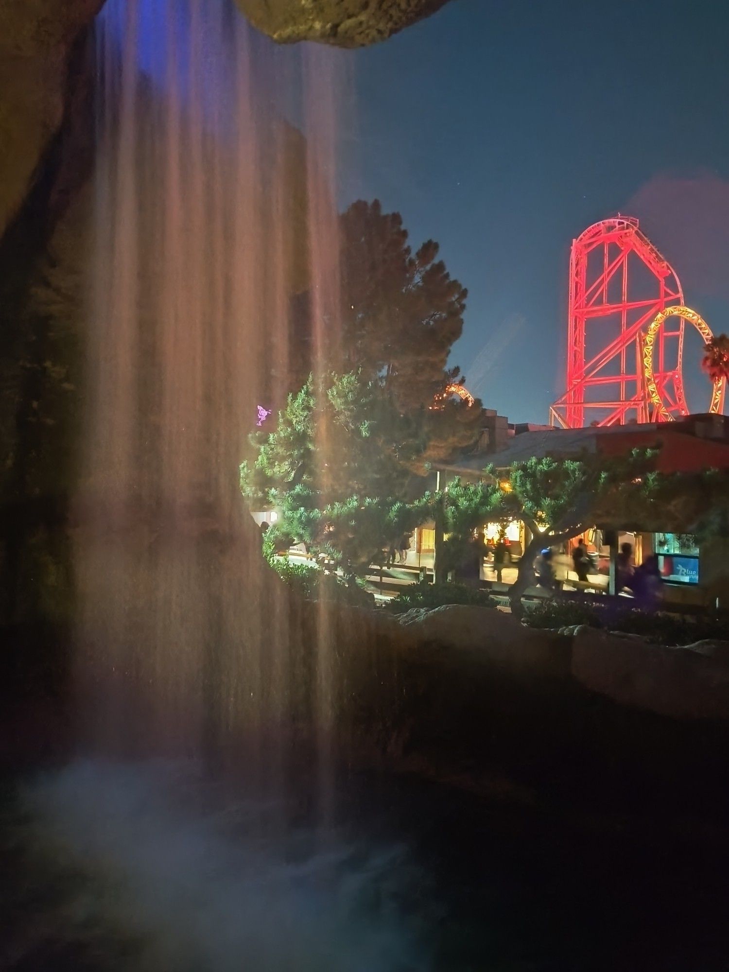 Photo of waterfall in Log Ride queue and HangTime roller coaster lit up in red lights.