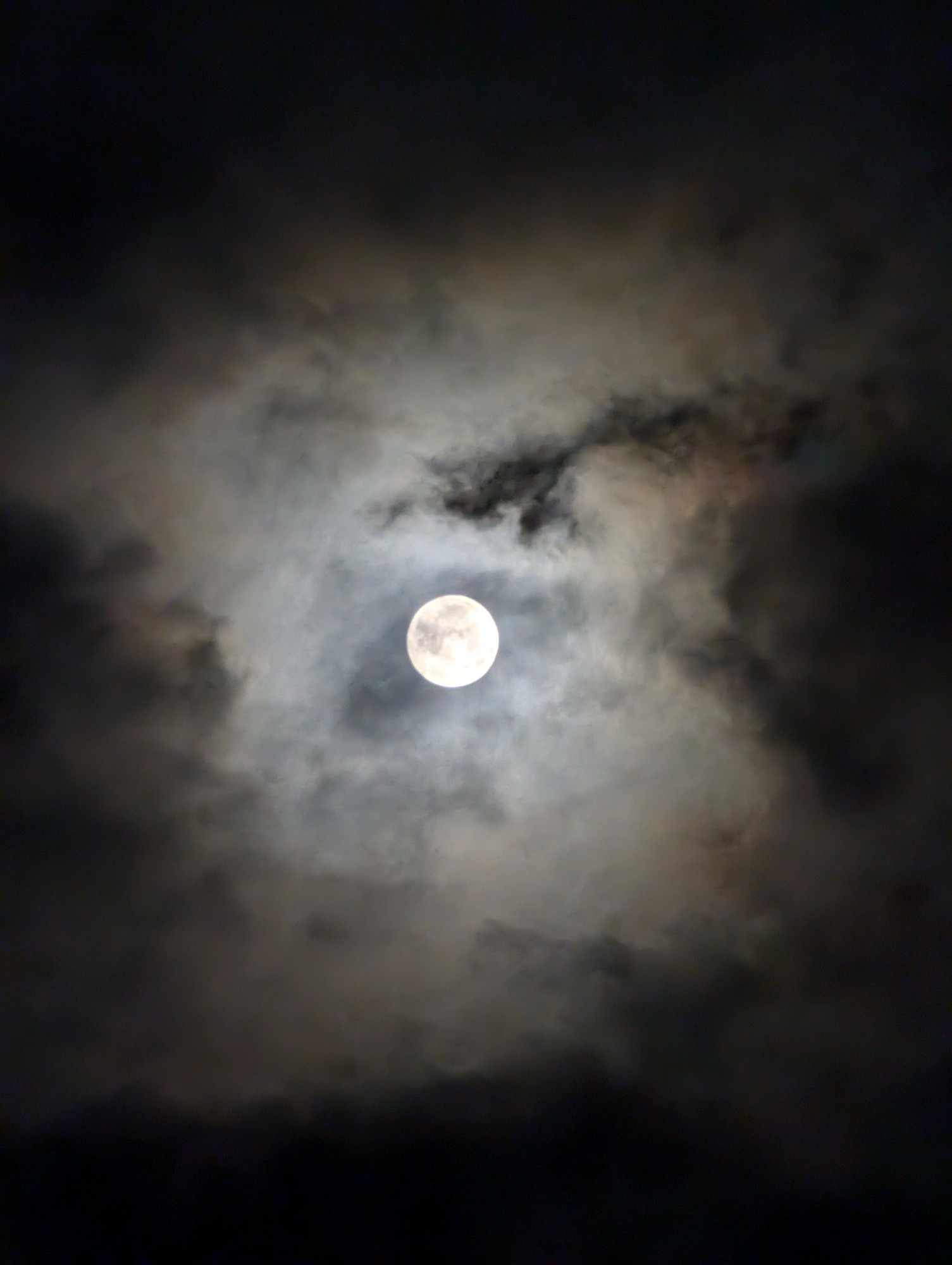 A picture of the full moon with warm clouds around it