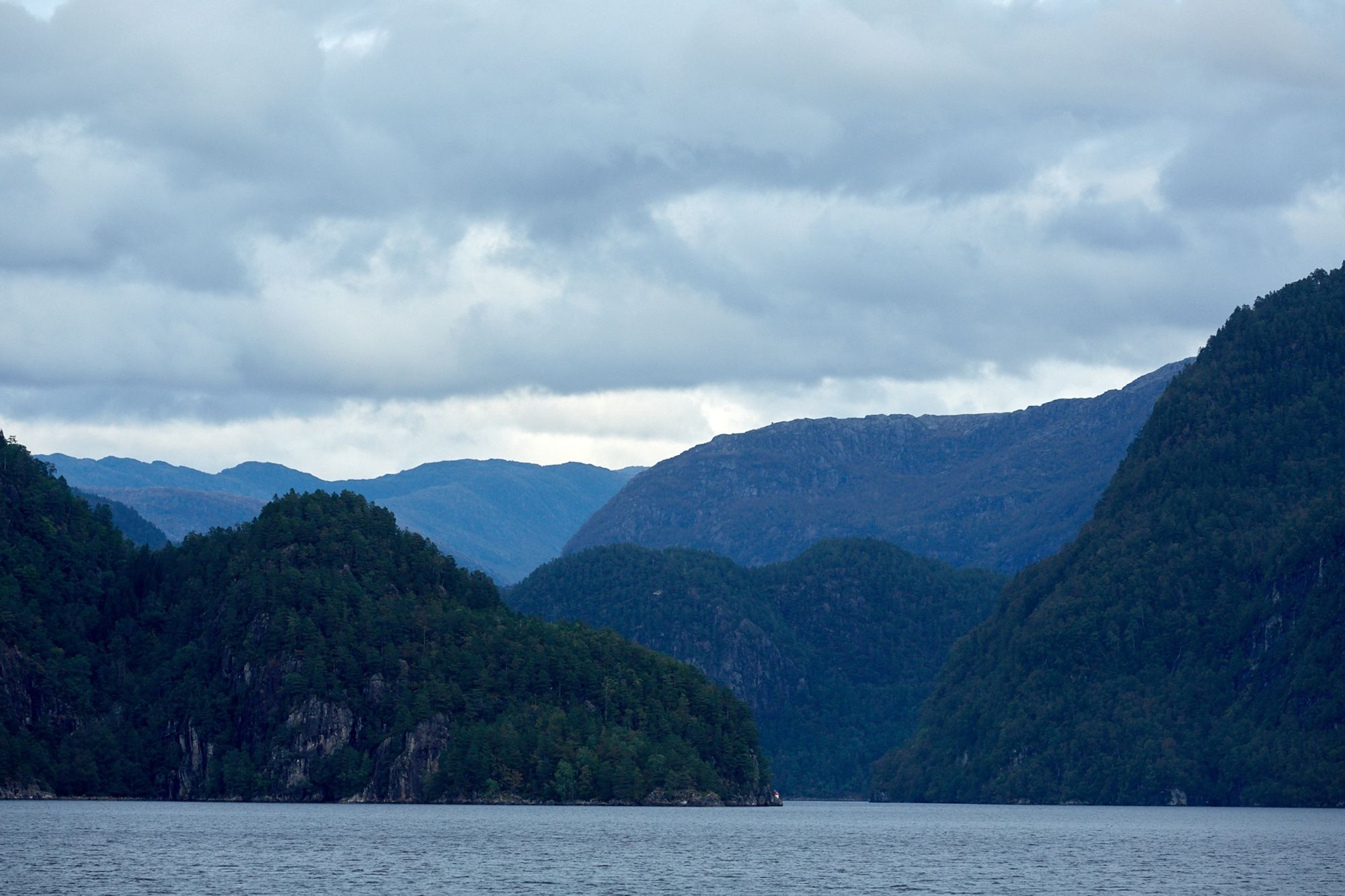 Steep landscapes covered in trees surrounding a sea. Clouds overhead