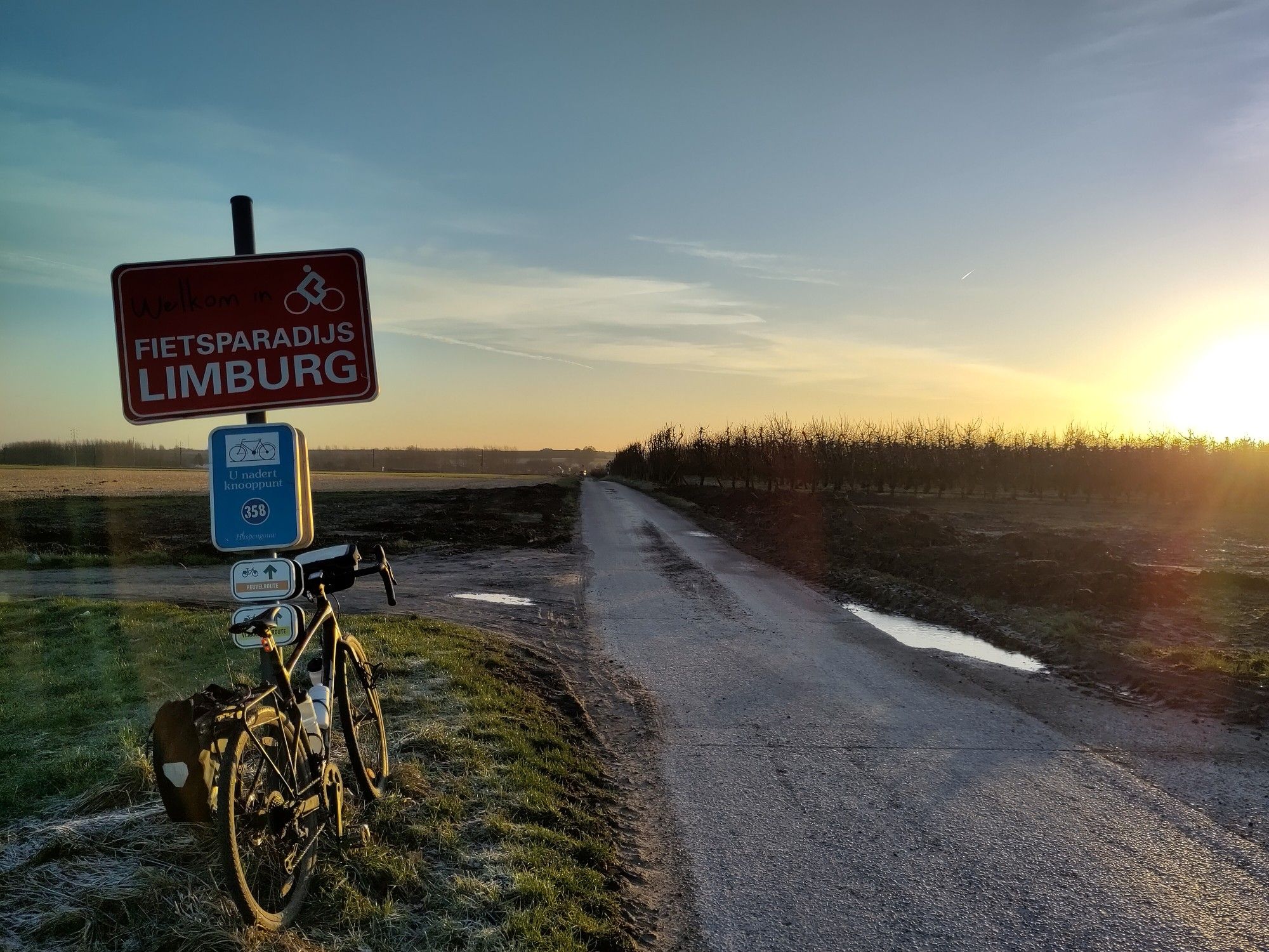 Vélo posé contre un panneau "Fietsparadijs Limburg", au lever de soleil.