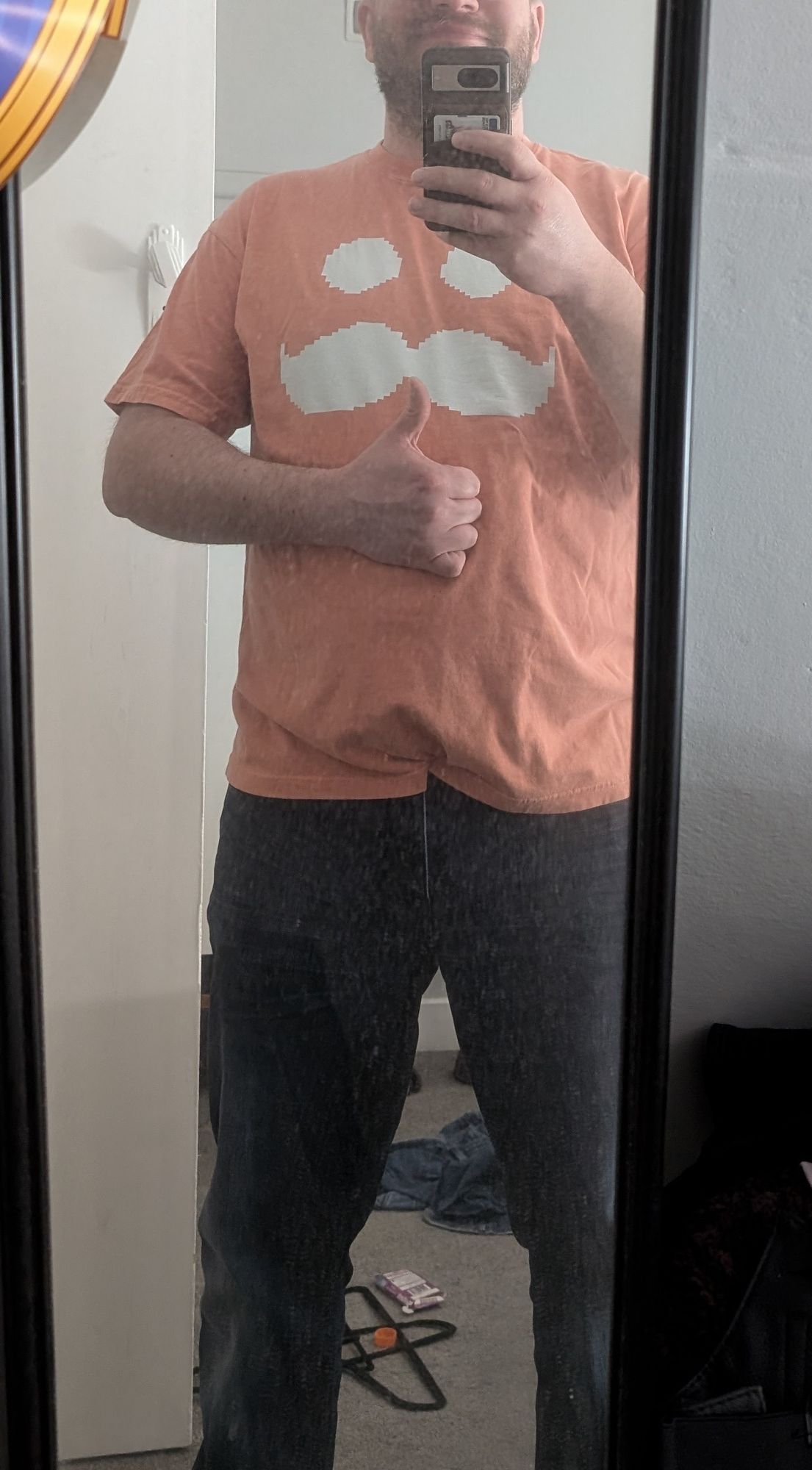 Drew wearing an orange tshirt with the image of two eyes and a moustache in white.