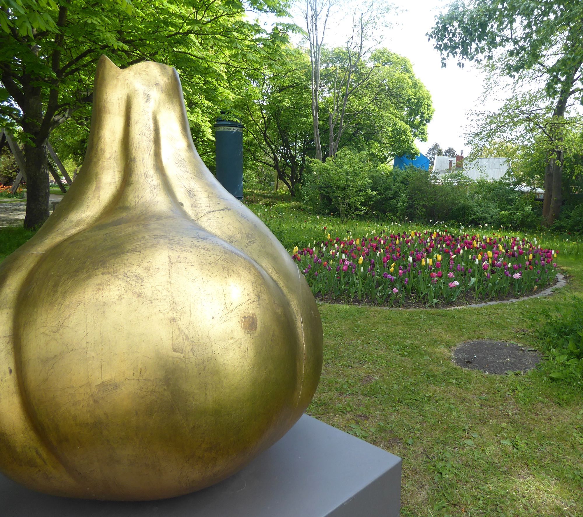 At Tulipan in Berlin's Britzer Garten. In the foreground a golden statue of a tulip bulb. In the background a formal tulip bed in front of trees and shrubs.