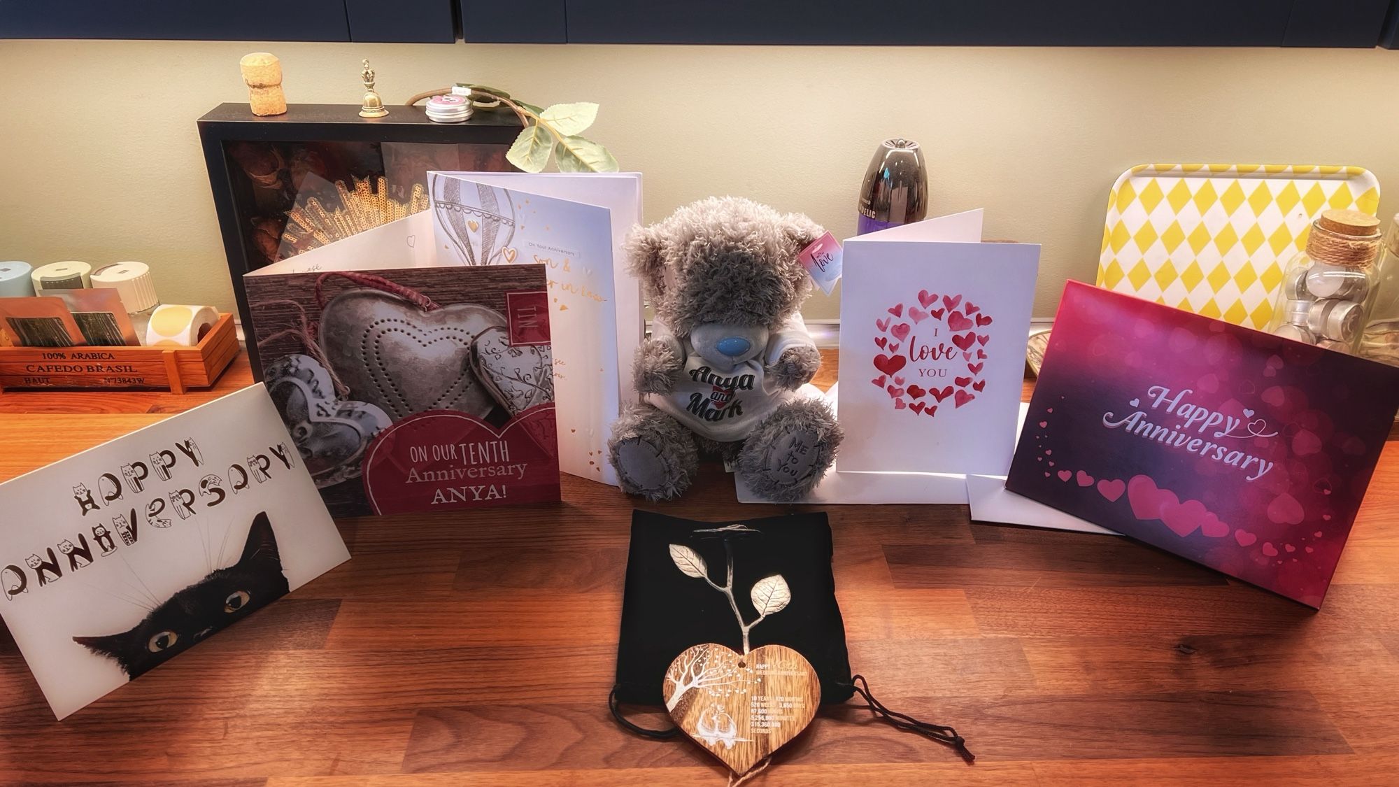 Wedding anniversary cards on a table surrounding two gifts in the middle, a teddy bear and a silver rose.