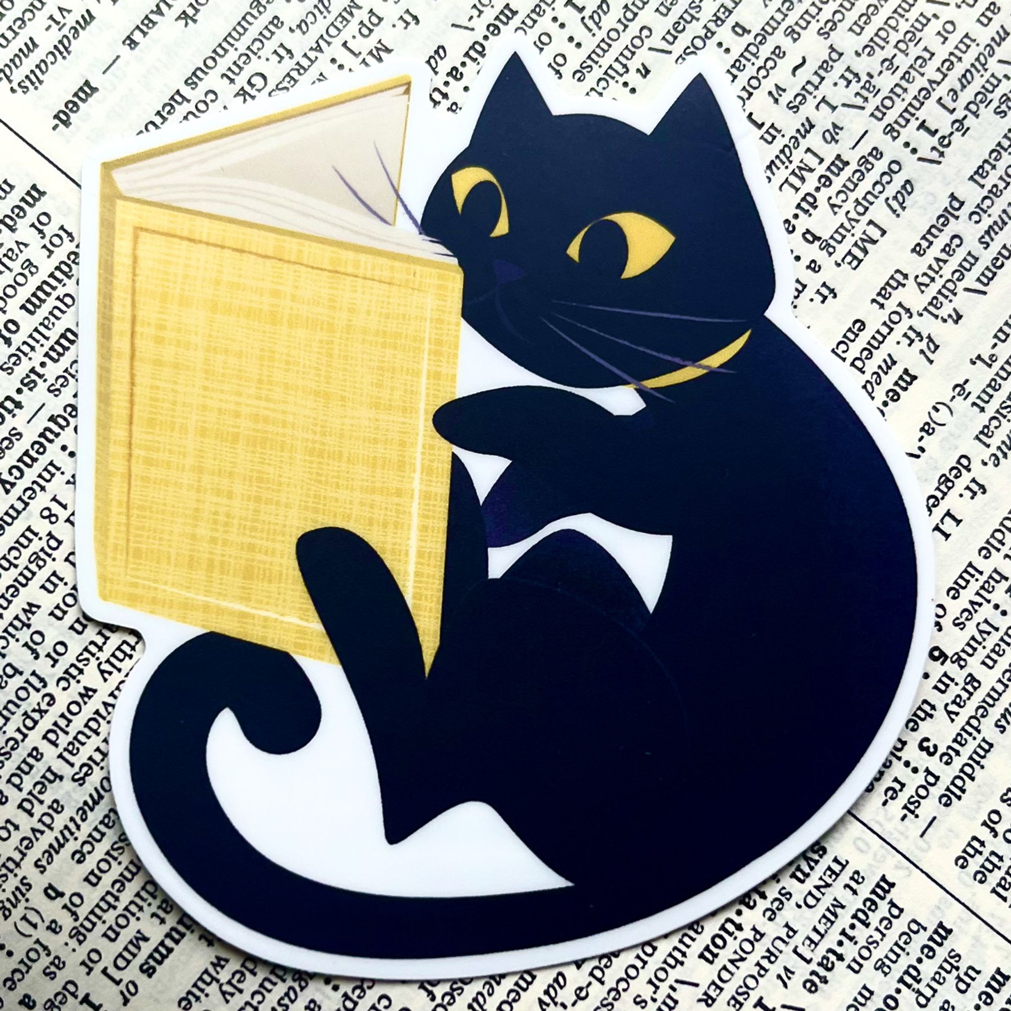 sticker of a black cat reading a yellow book