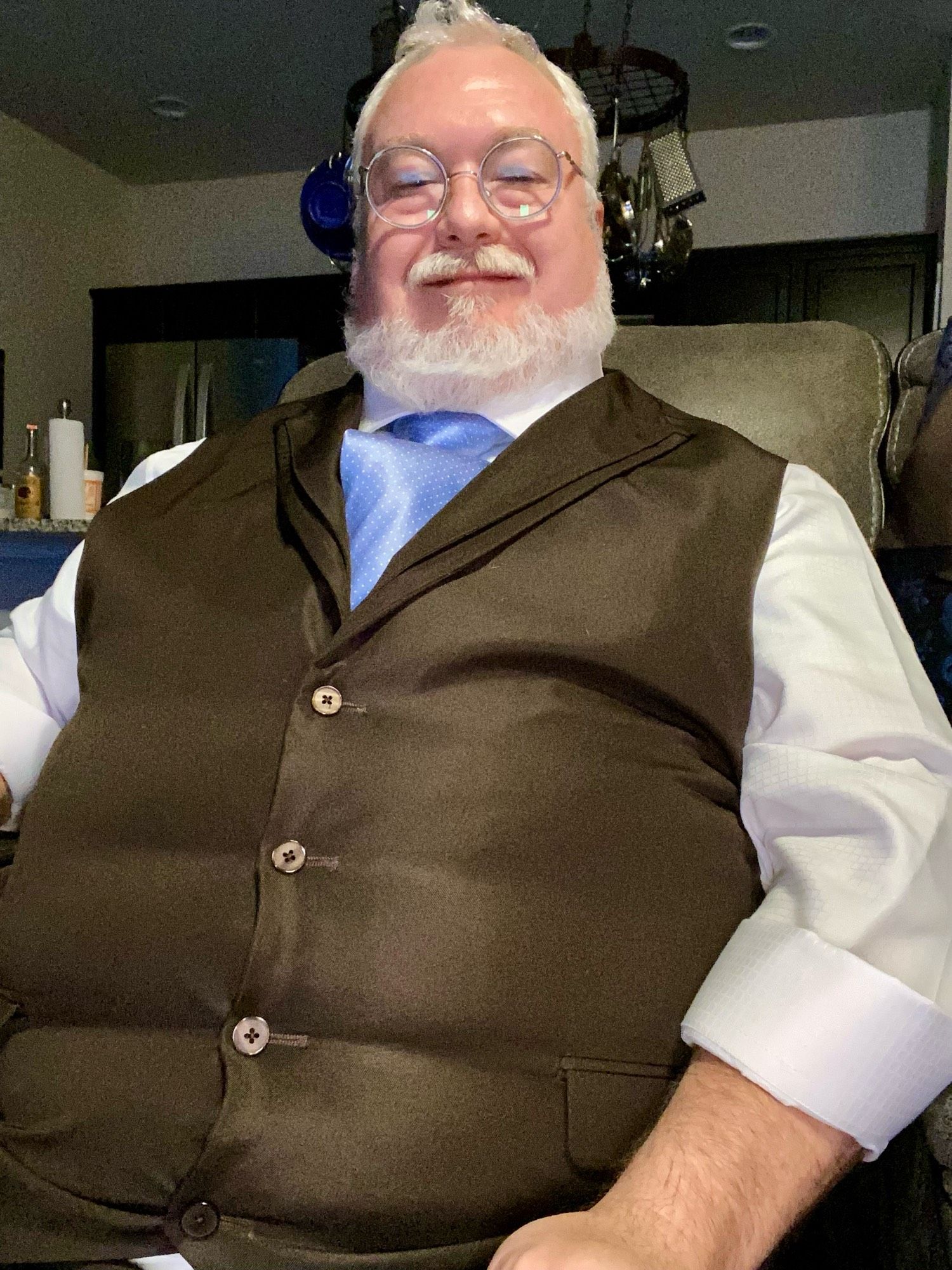 Chubby gray haired man, in a tight vest and shiny sky blue white pin dot tie. The vest buttons a straining.